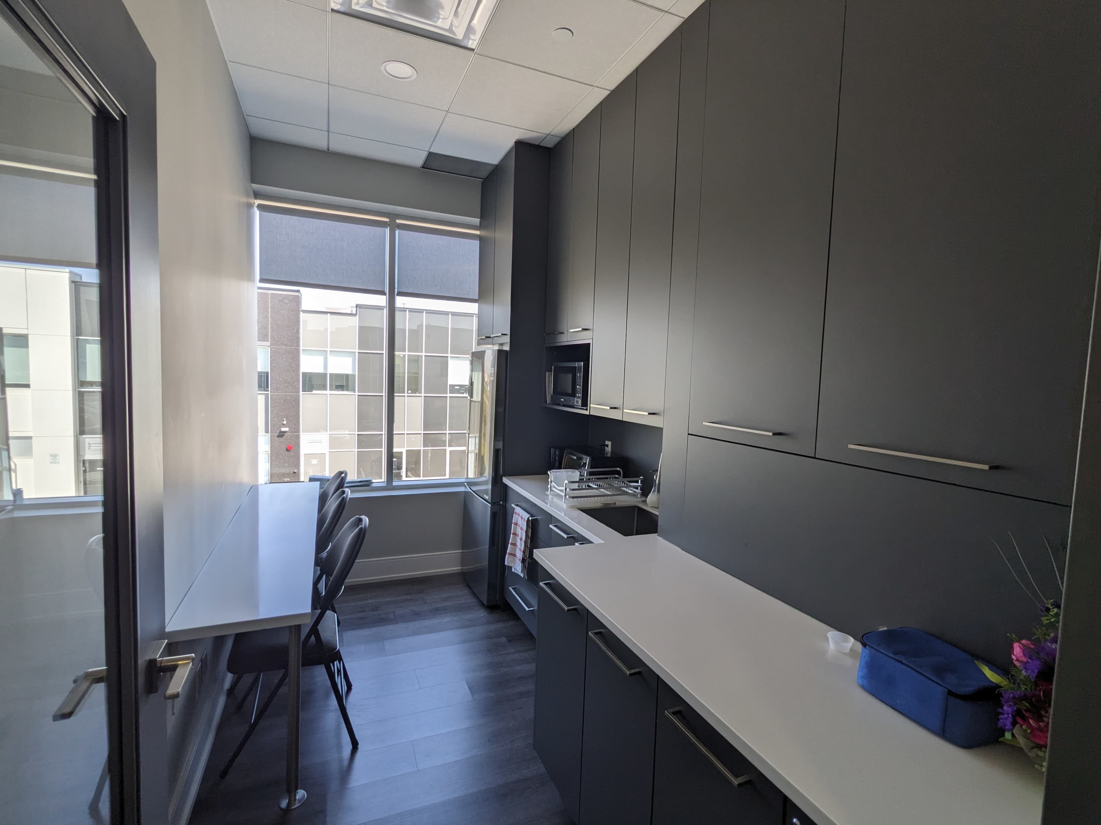 A modern kitchen with dark cabinets, a microwave, and a small table with chairs located near large windows.