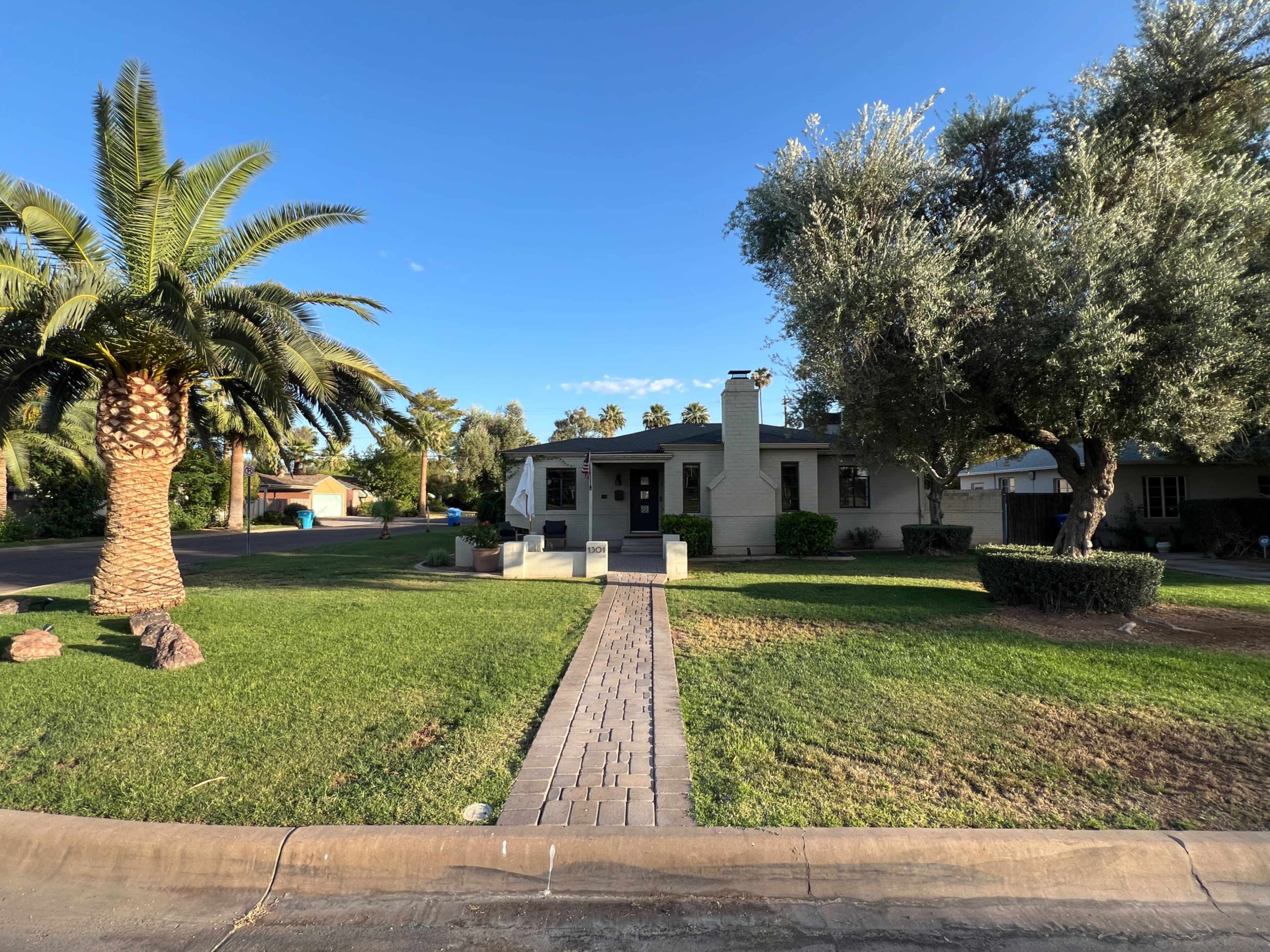 A single-story house with a front pathway leads to the entrance, surrounded by palm trees and well-maintained lawn.