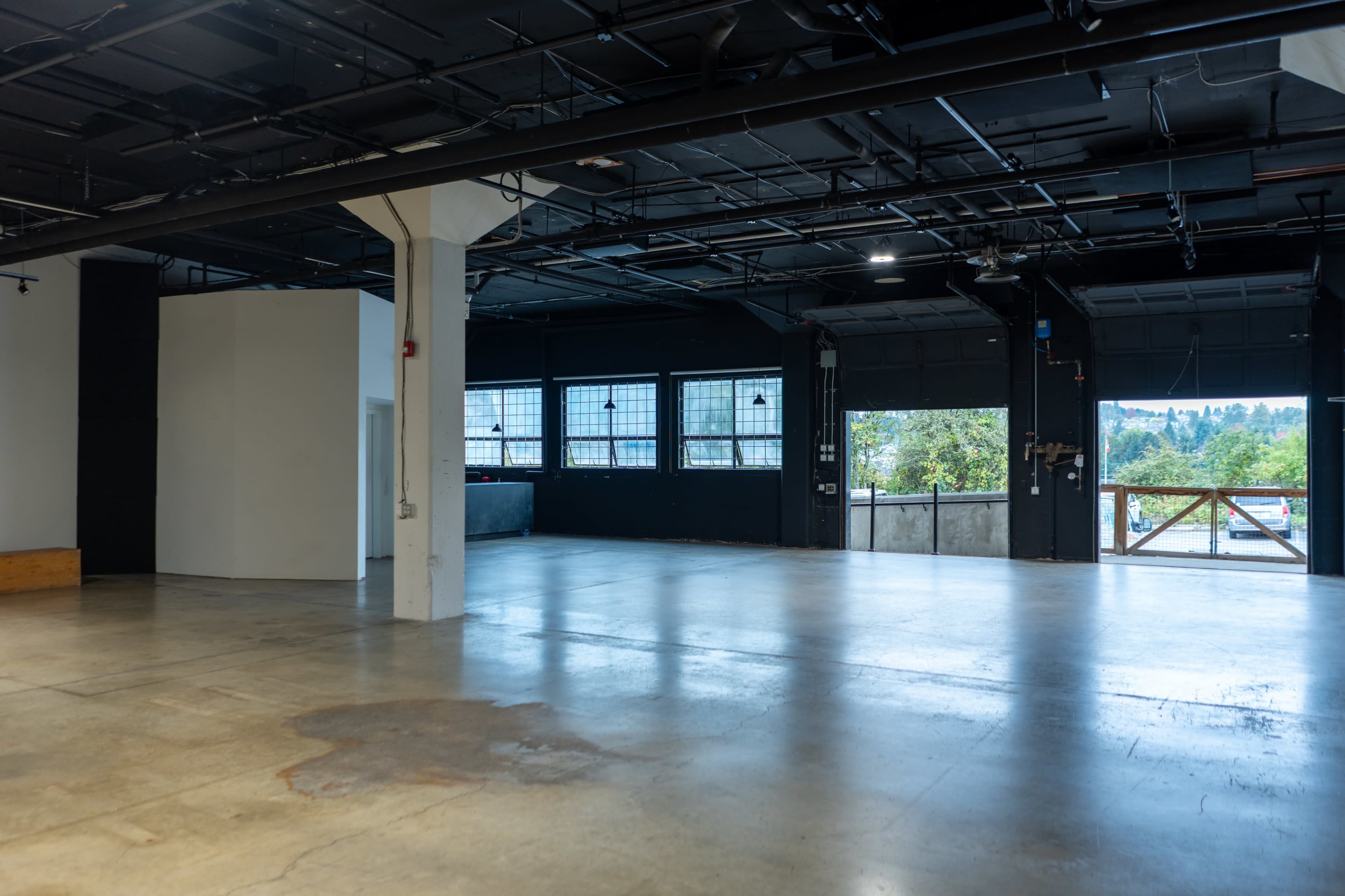 The image shows a spacious, empty industrial-style room with large windows and concrete flooring.