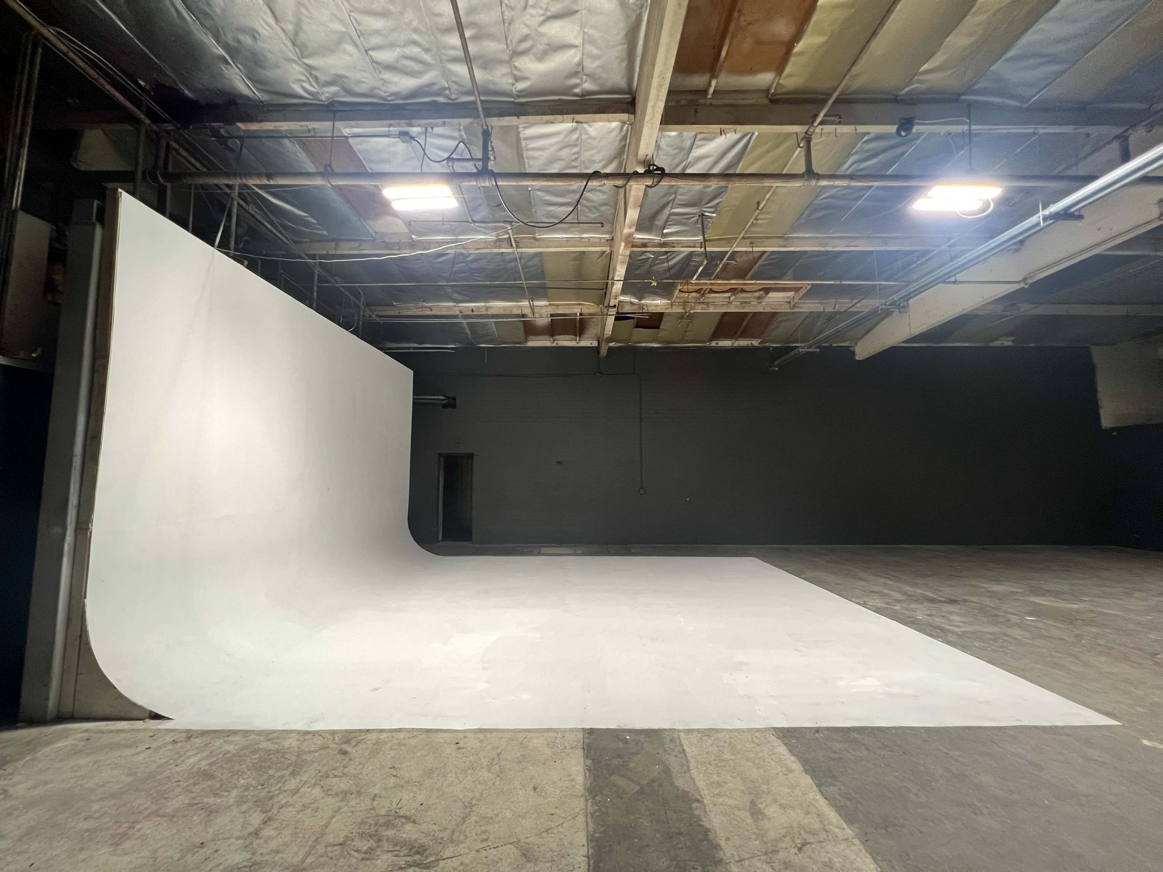 A spacious studio with a large white backdrop and a smooth floor, illuminated by overhead lights.