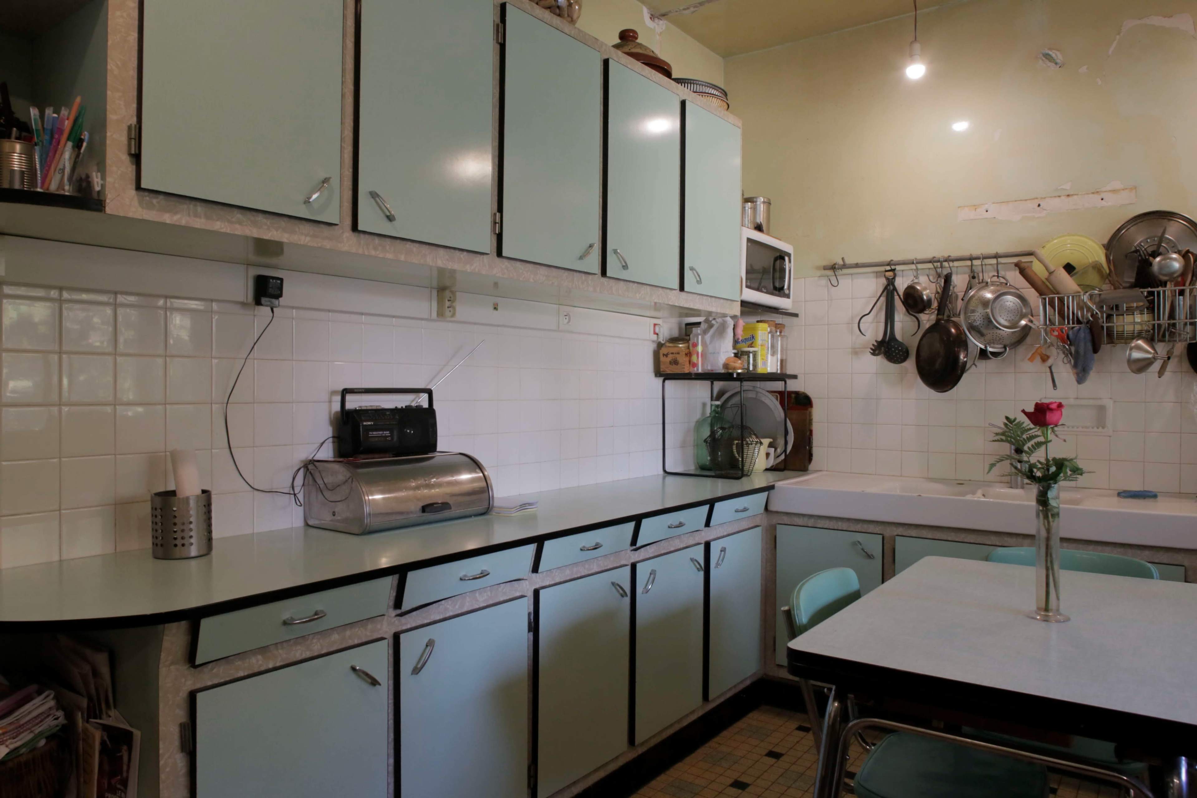 The image shows a retro-style kitchen with mint green cabinets, a countertop, and hanging utensils.