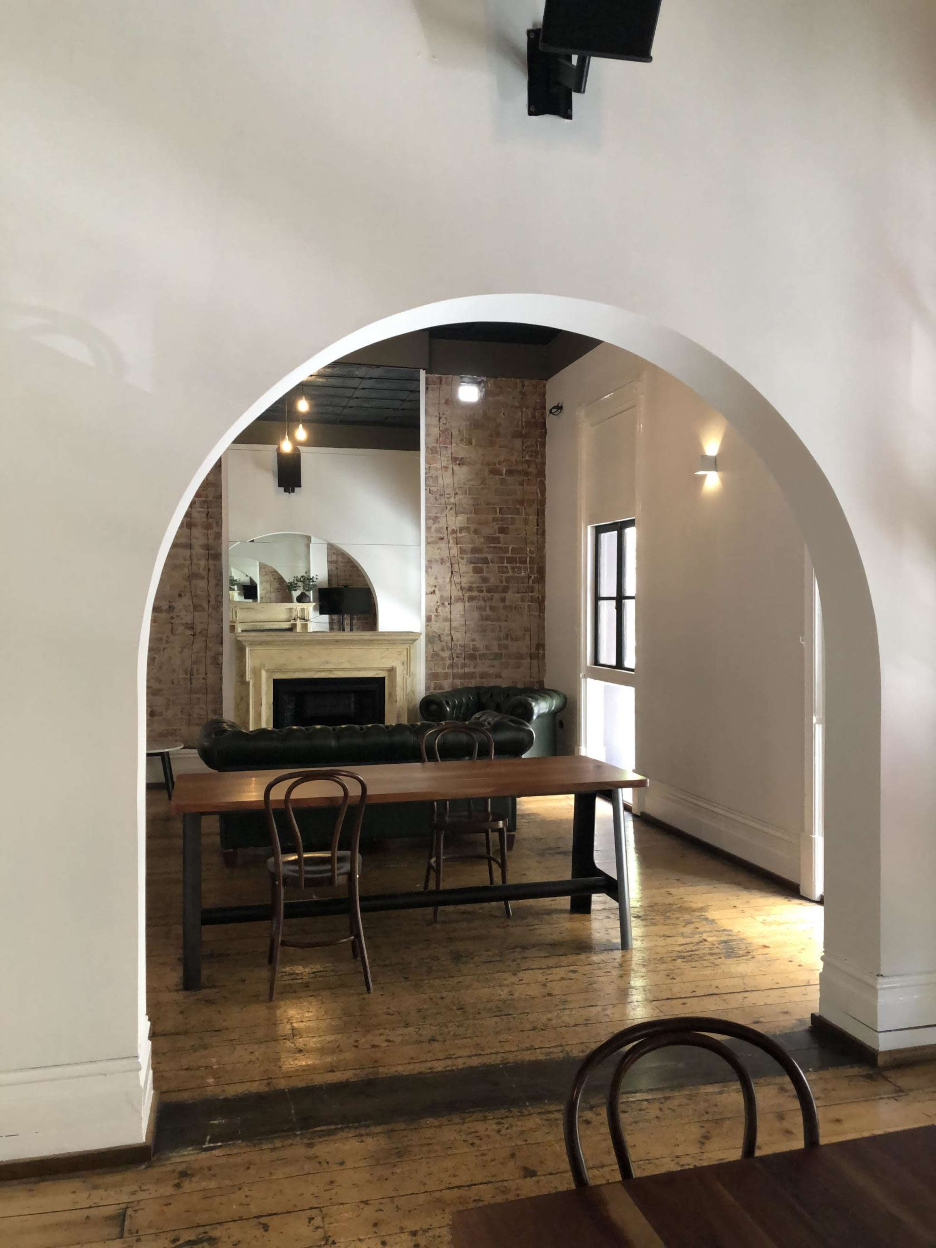 A spacious dining area features a large wooden table and a green leather sofa visible through an arched entrance.