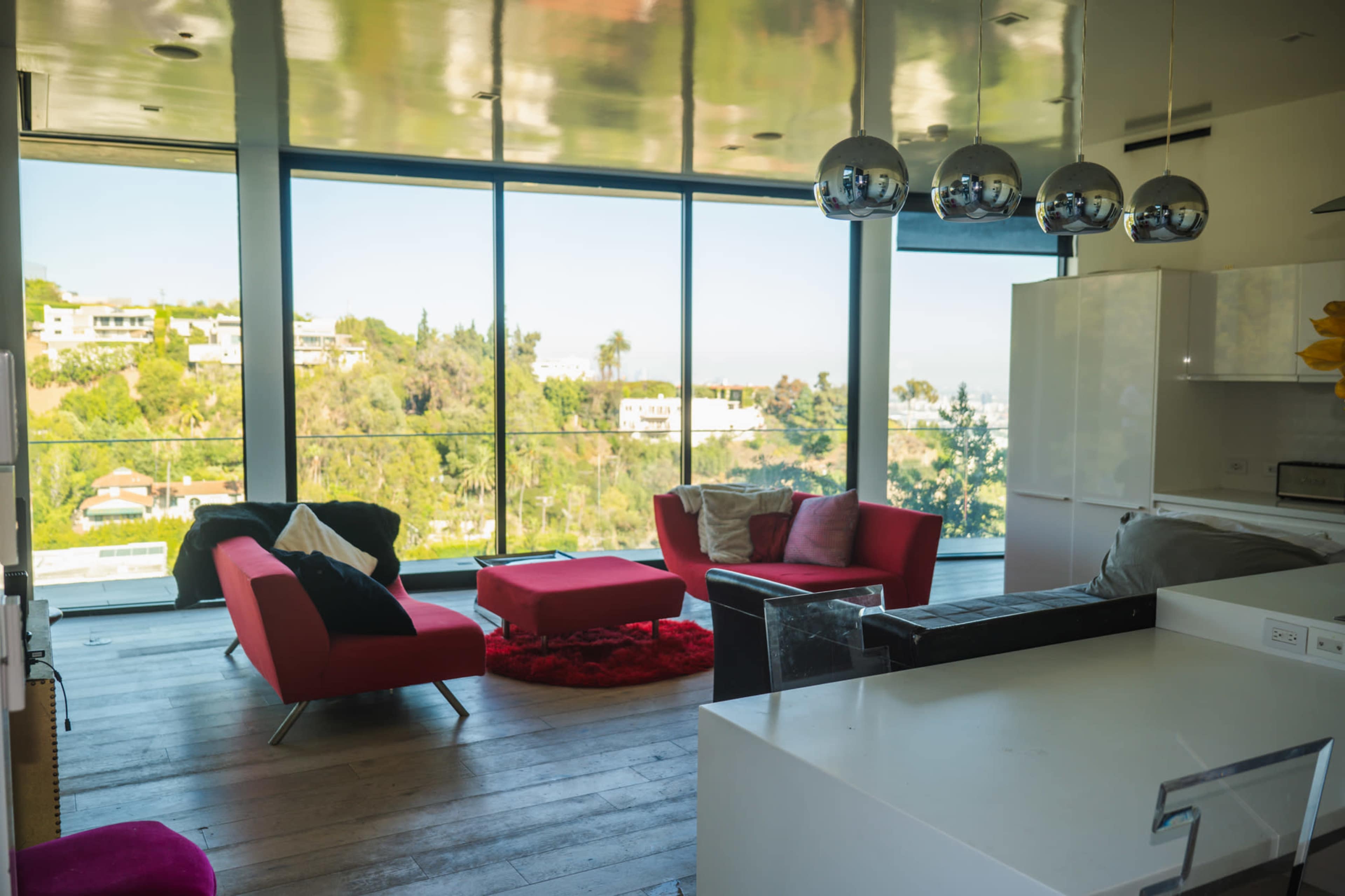 A modern living room features red furniture and large windows that overlook a green hillside.