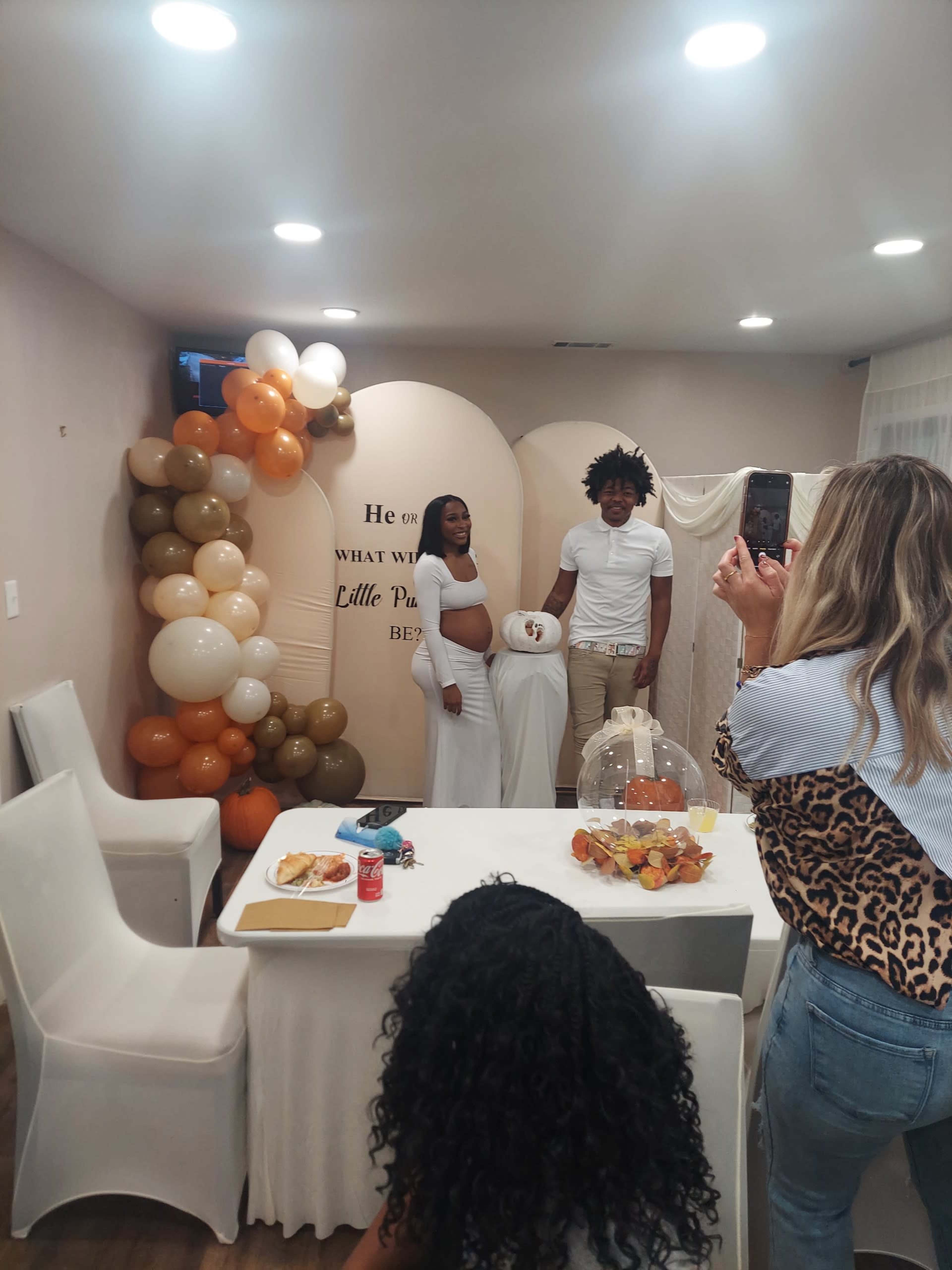 A couple poses for a photo at a celebration, surrounded by decorative balloons and a dessert table.