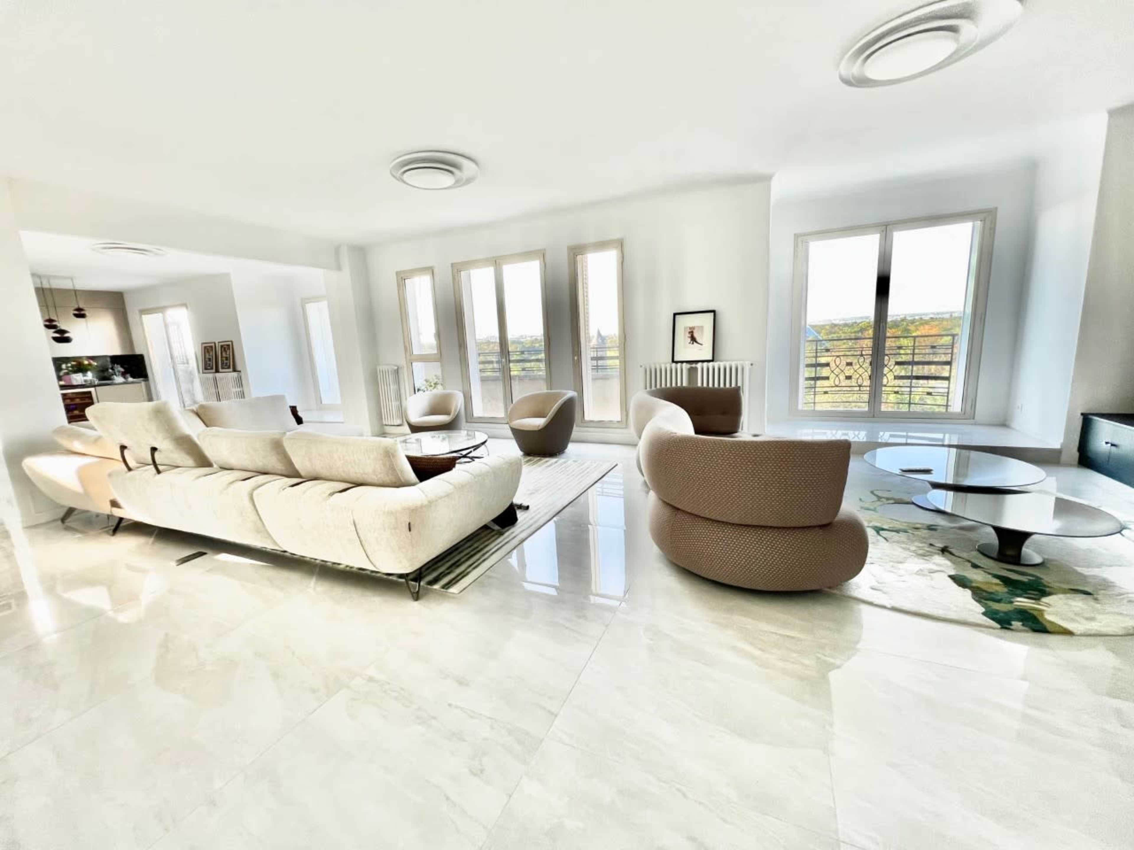 A spacious living room featuring modern furniture, large windows, and a marble floor.
