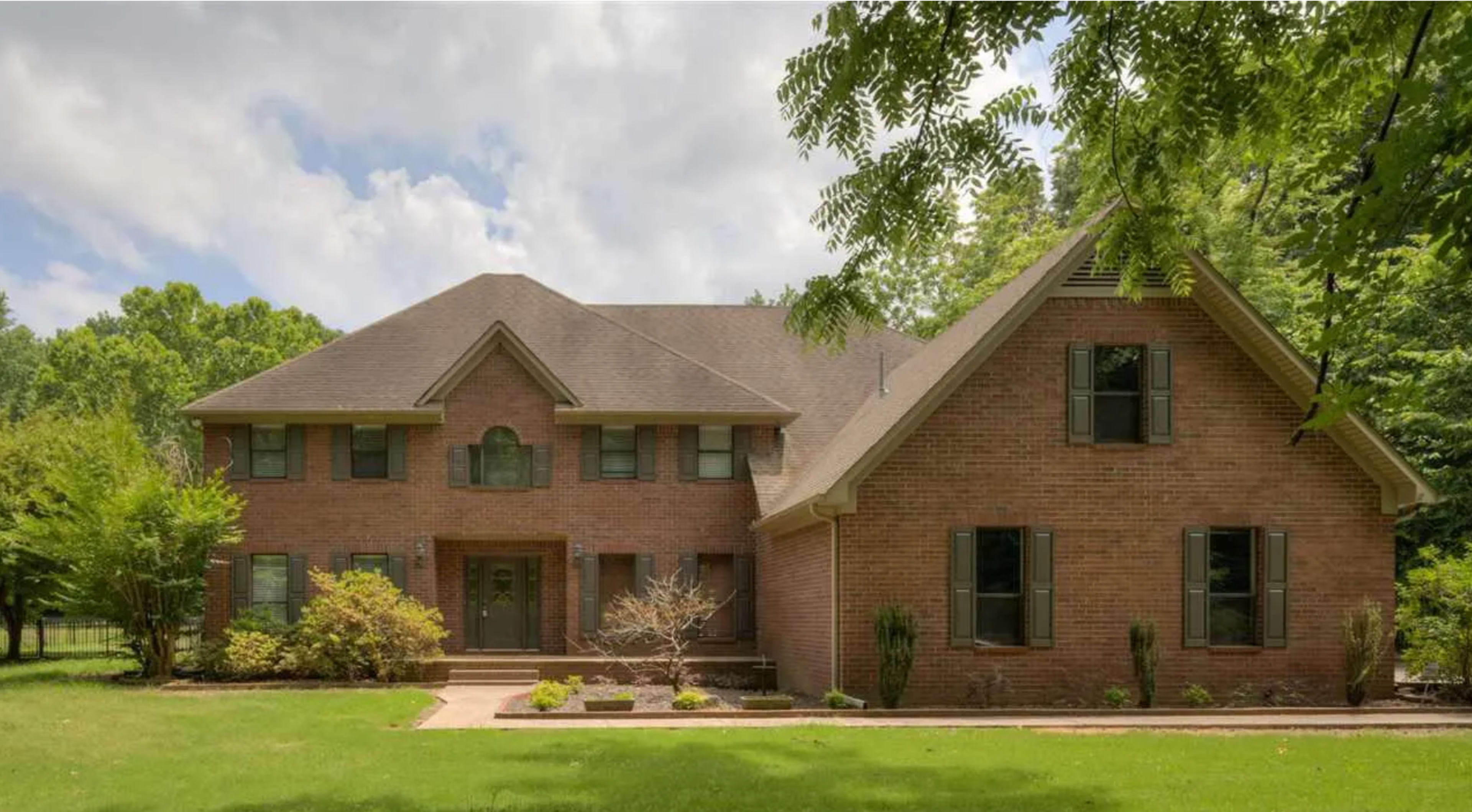 A large two-story brick house with a landscaped front yard and a mixture of symmetrical and asymmetrical architectural features.