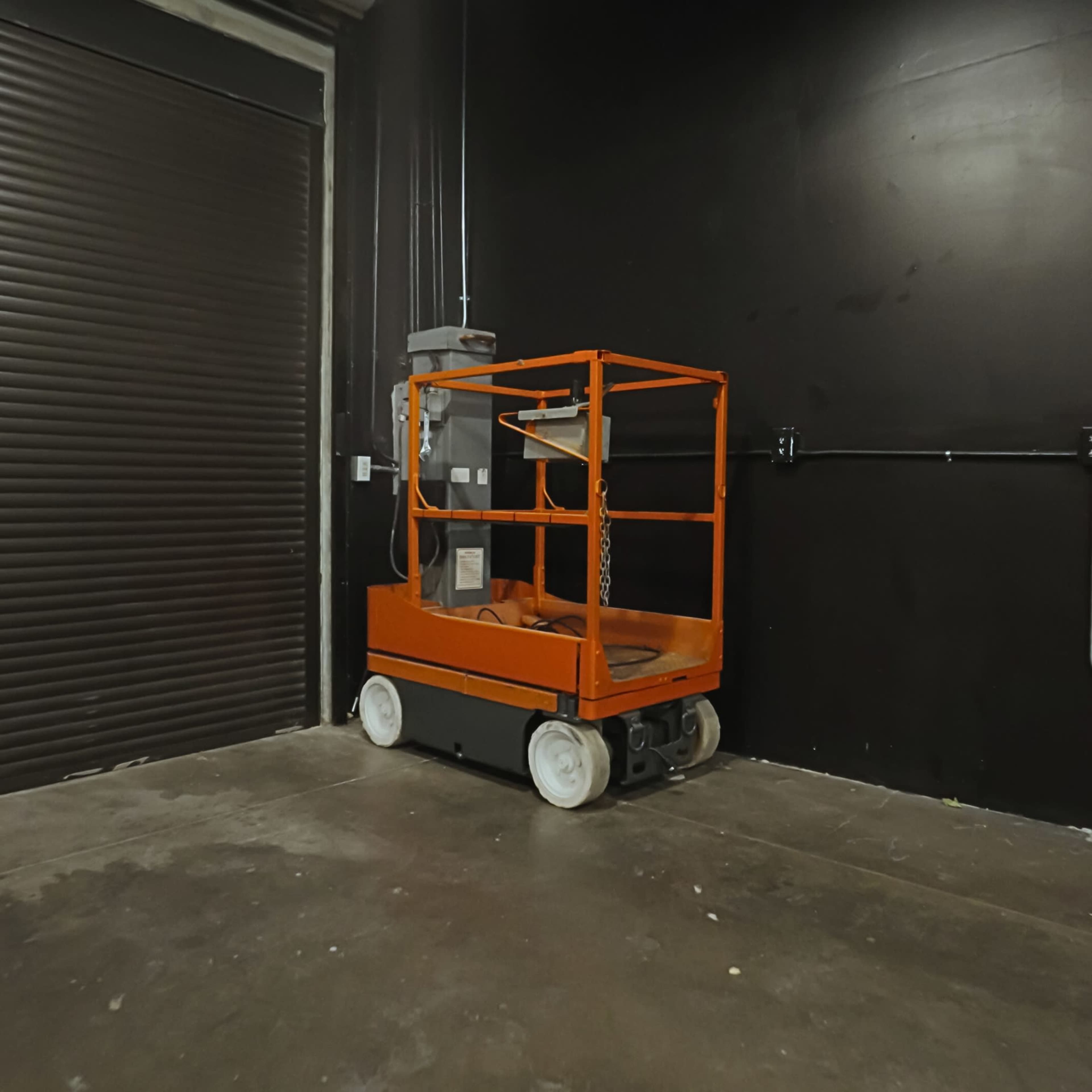 An orange lift platform with a safety guardrail is parked in a dimly lit garage.