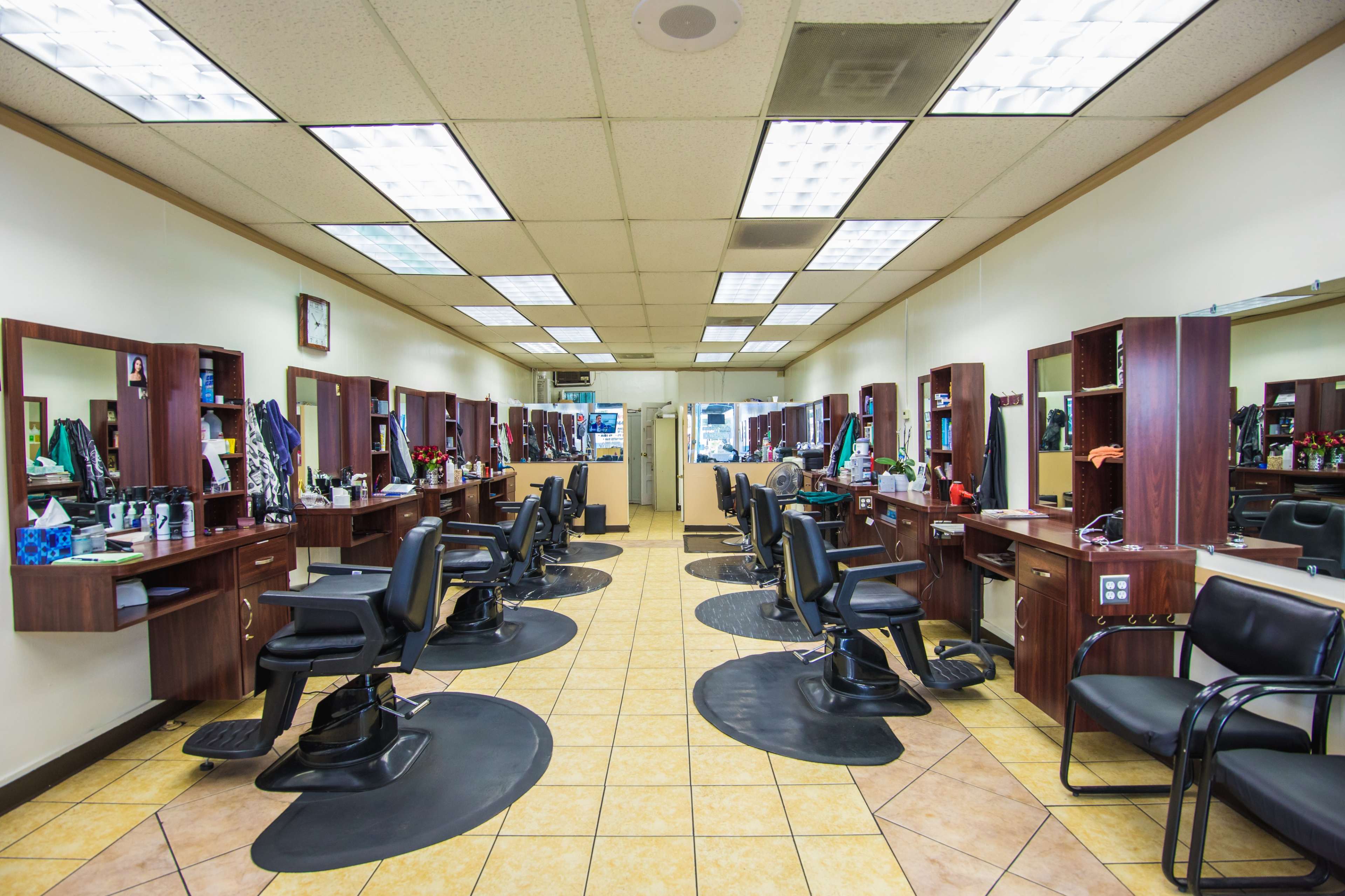 A hair salon with several styling stations, each equipped with mirrors and chairs, arranged in a symmetrical layout on a tiled floor.