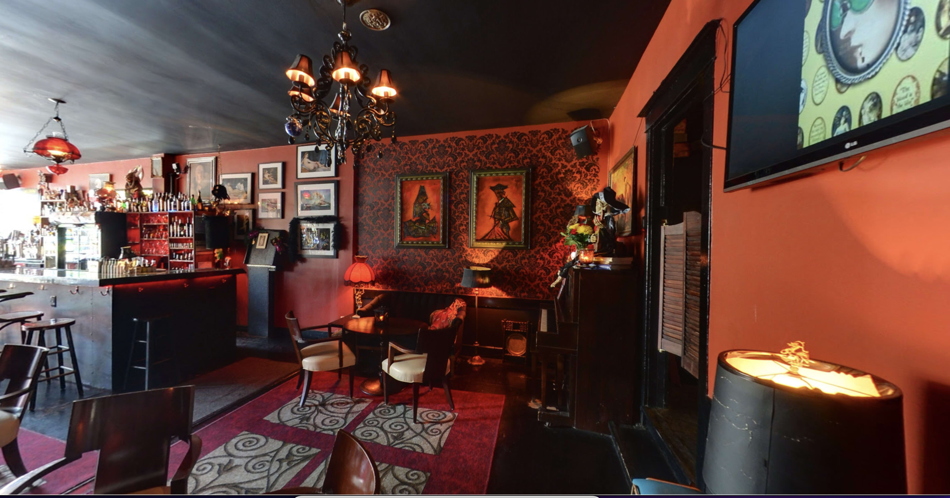 The image shows a dimly lit bar with decorative walls, a chandelier, and seating arrangements featuring a rug and framed art on the walls.