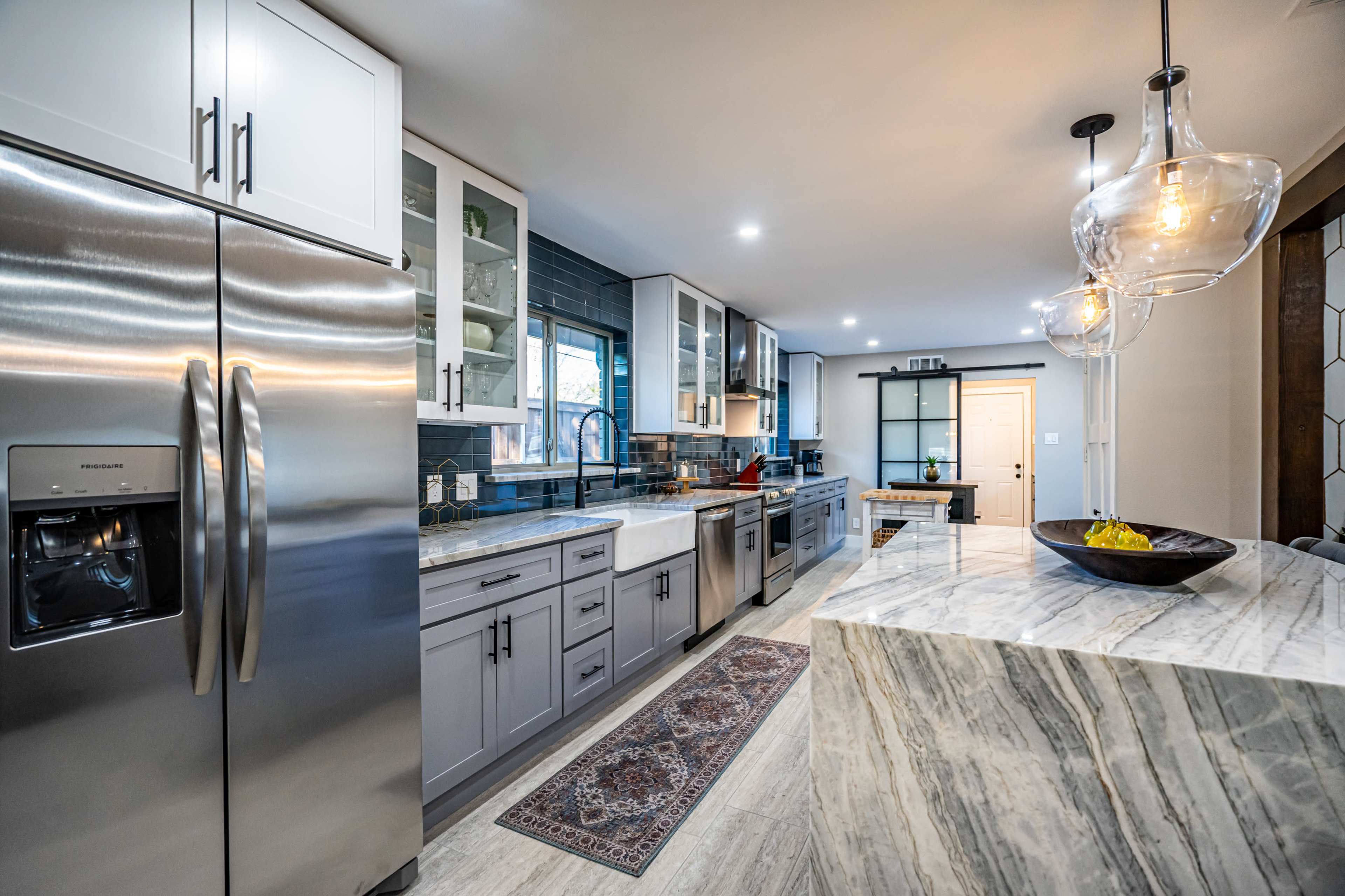 A modern kitchen with stainless steel appliances, a marble countertop, and white cabinetry.