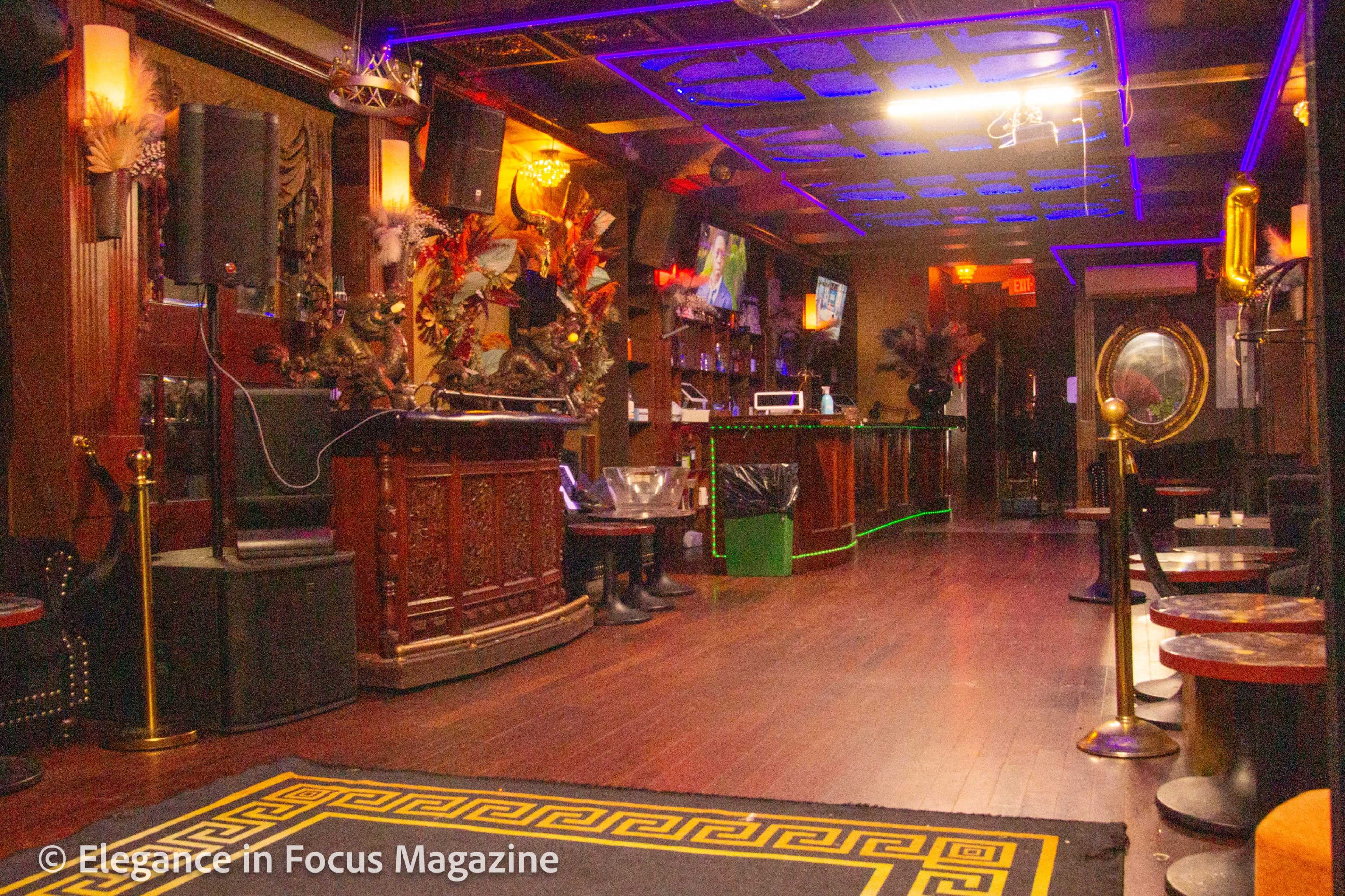 A dimly lit lounge with a bar area, seating arrangements, and decorative elements including neon lighting and patterned flooring.