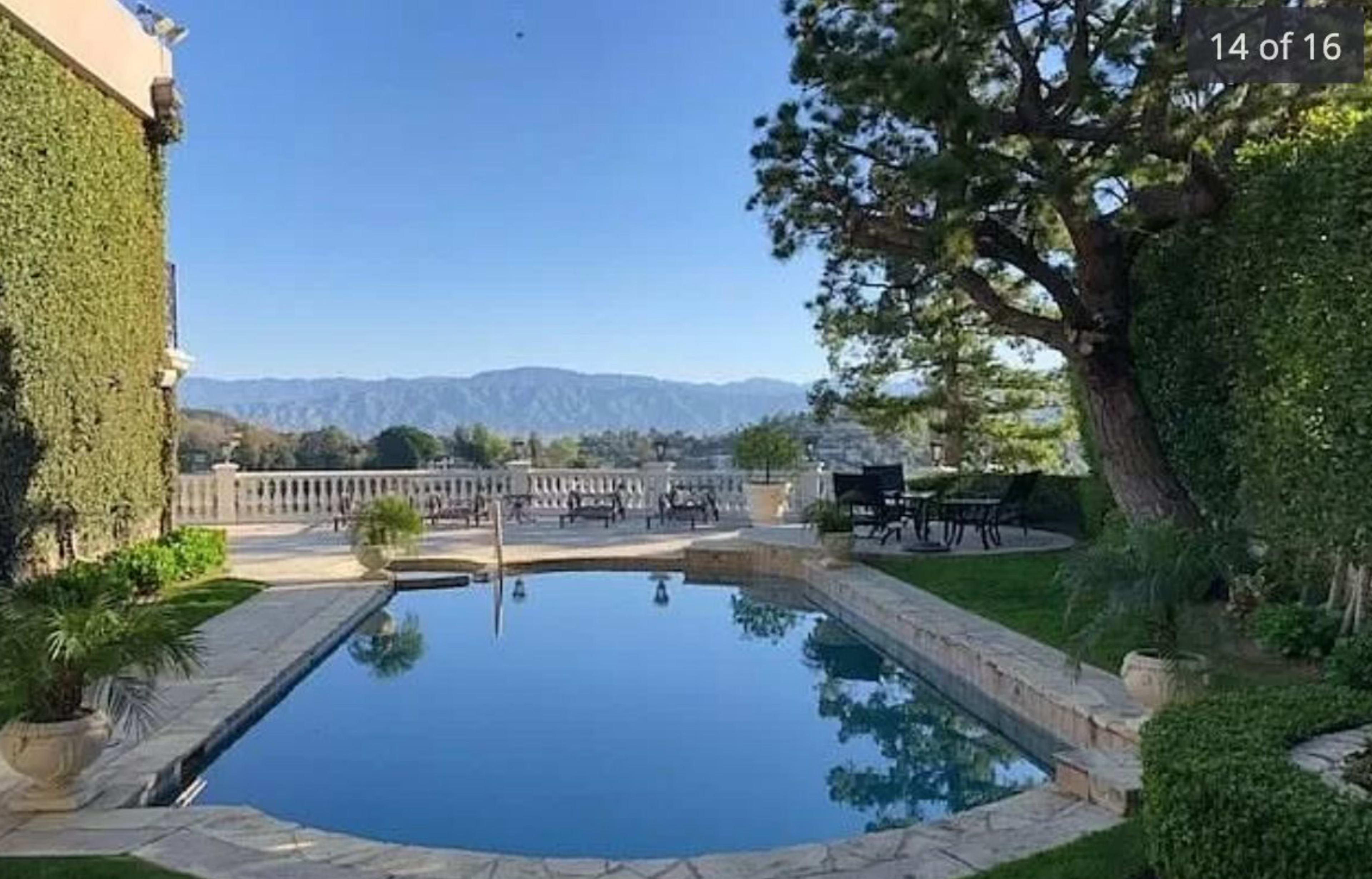 A swimming pool surrounded by greenery and mountains in the background.