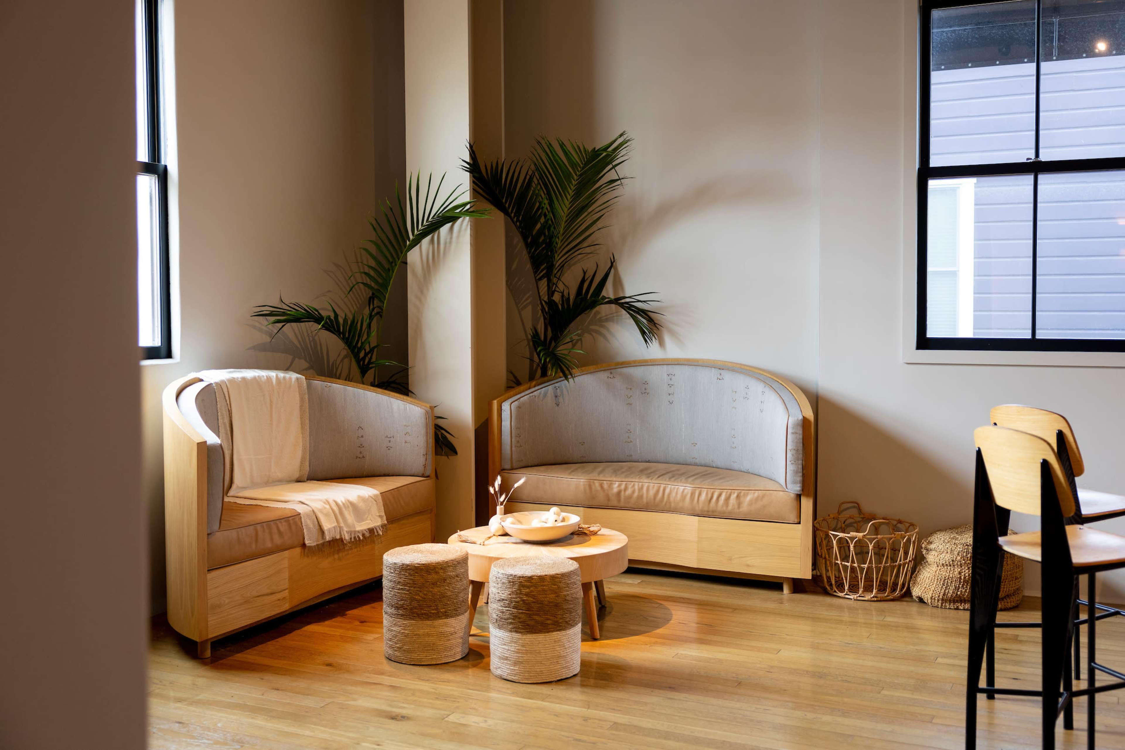 A cozy seating area features two wooden sofas with light cushions, accompanied by a small round table and decorative plants.