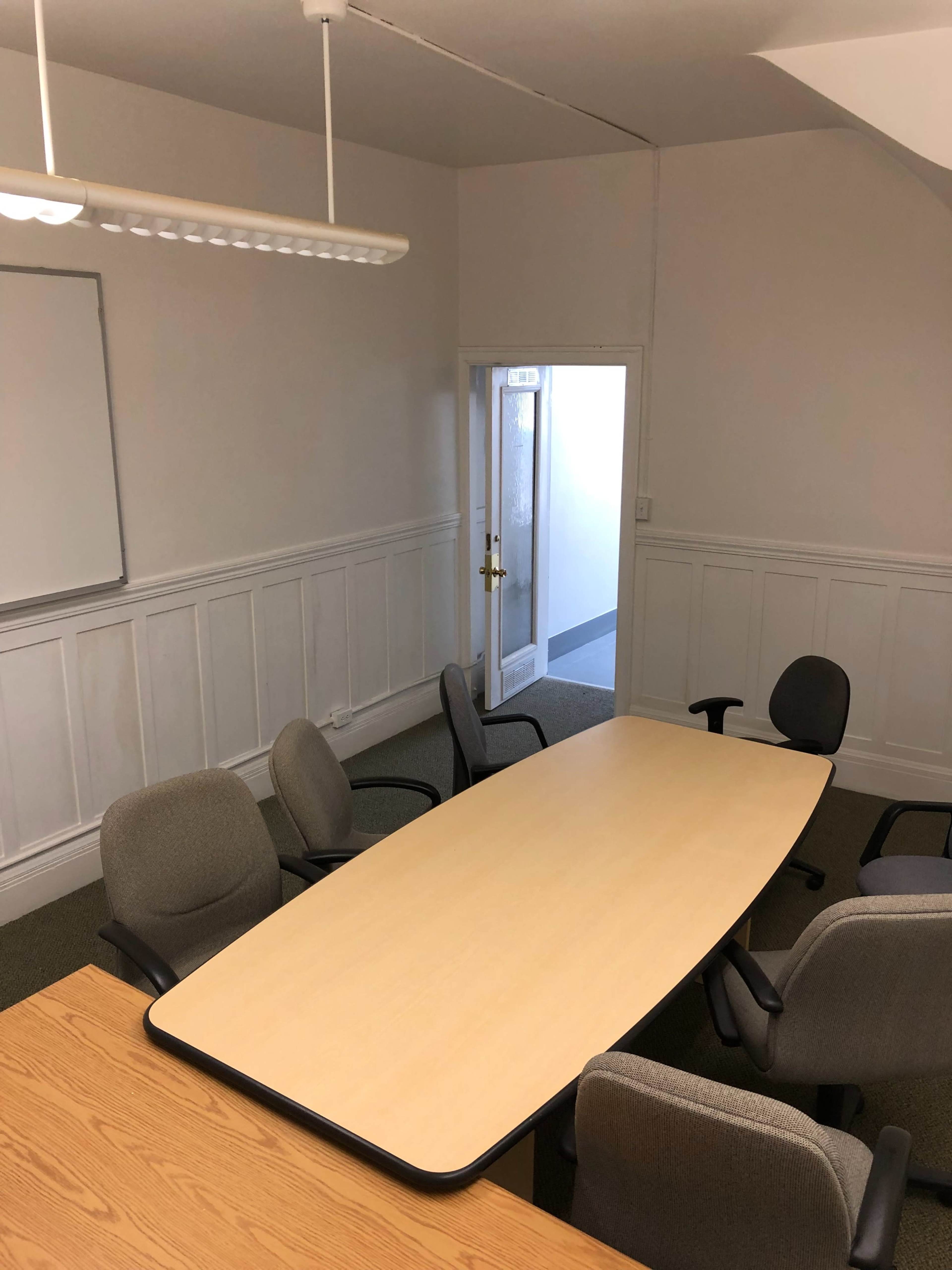 A conference room with a large oval table surrounded by several chairs and a whiteboard on the wall.