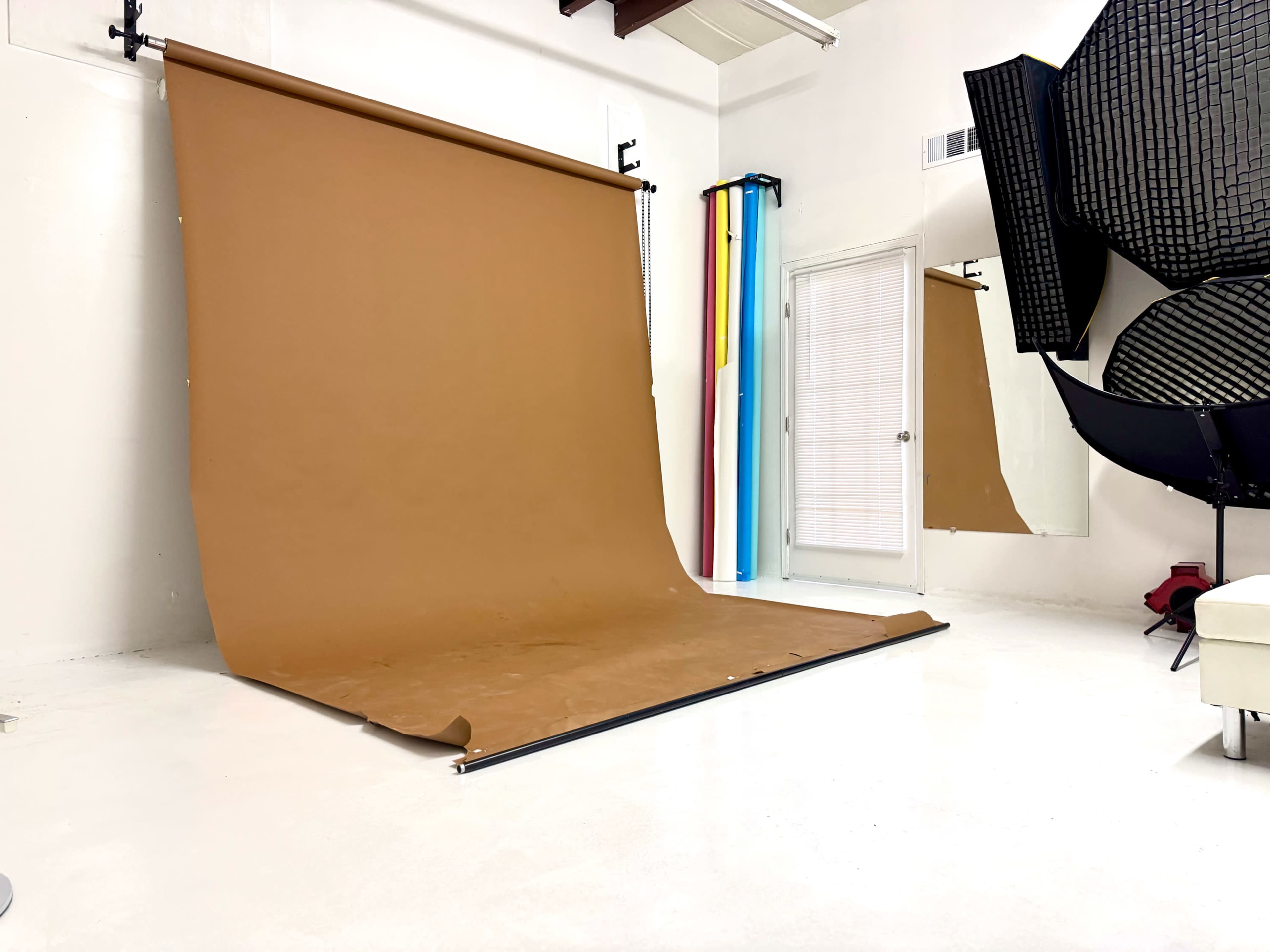 A photo studio features a brown backdrop with various colorful lighting equipment and a large reflector on one side.