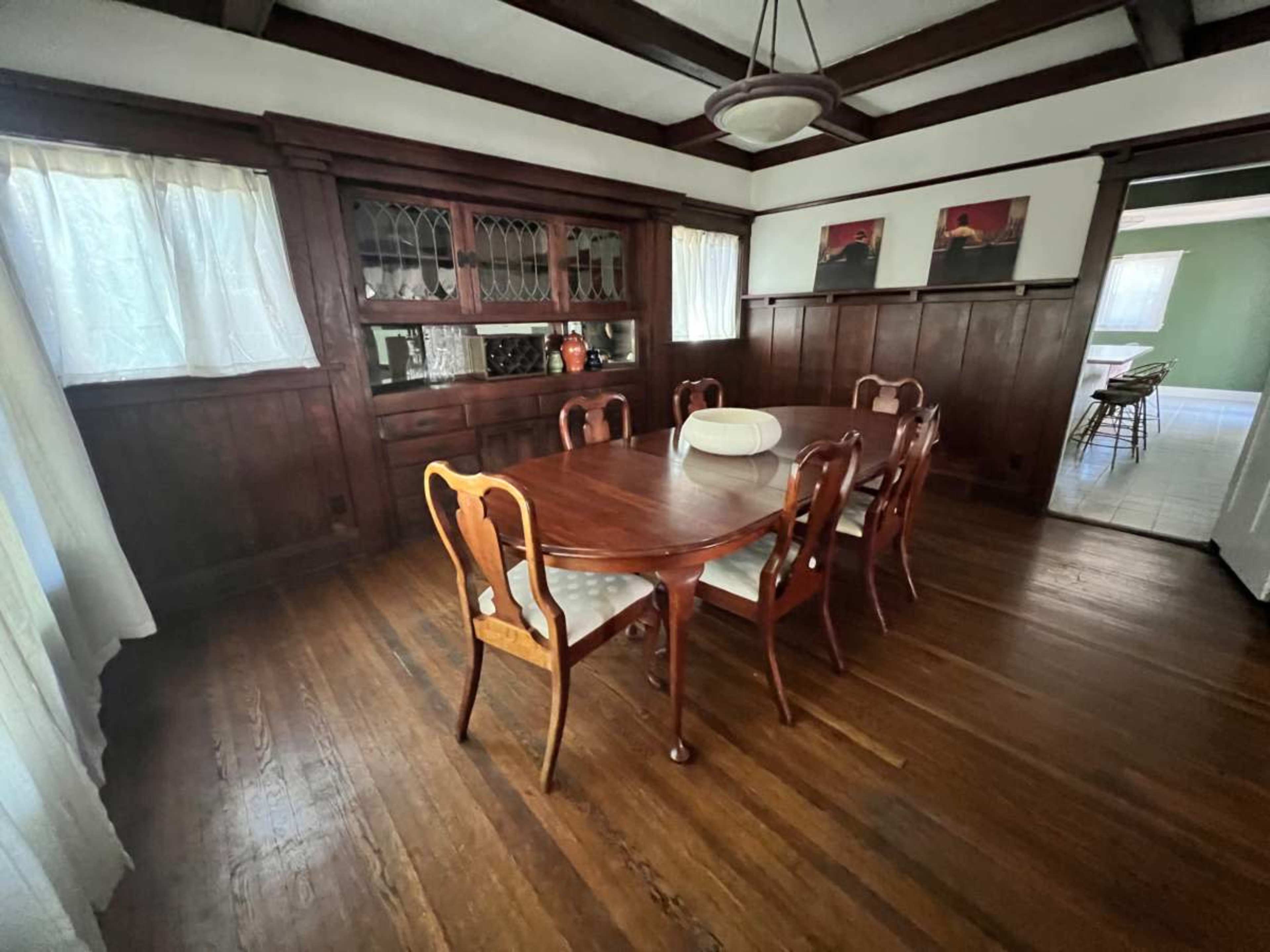 The image shows a dining room with a wooden table and chairs, a china cabinet, and a view into another room with green walls.