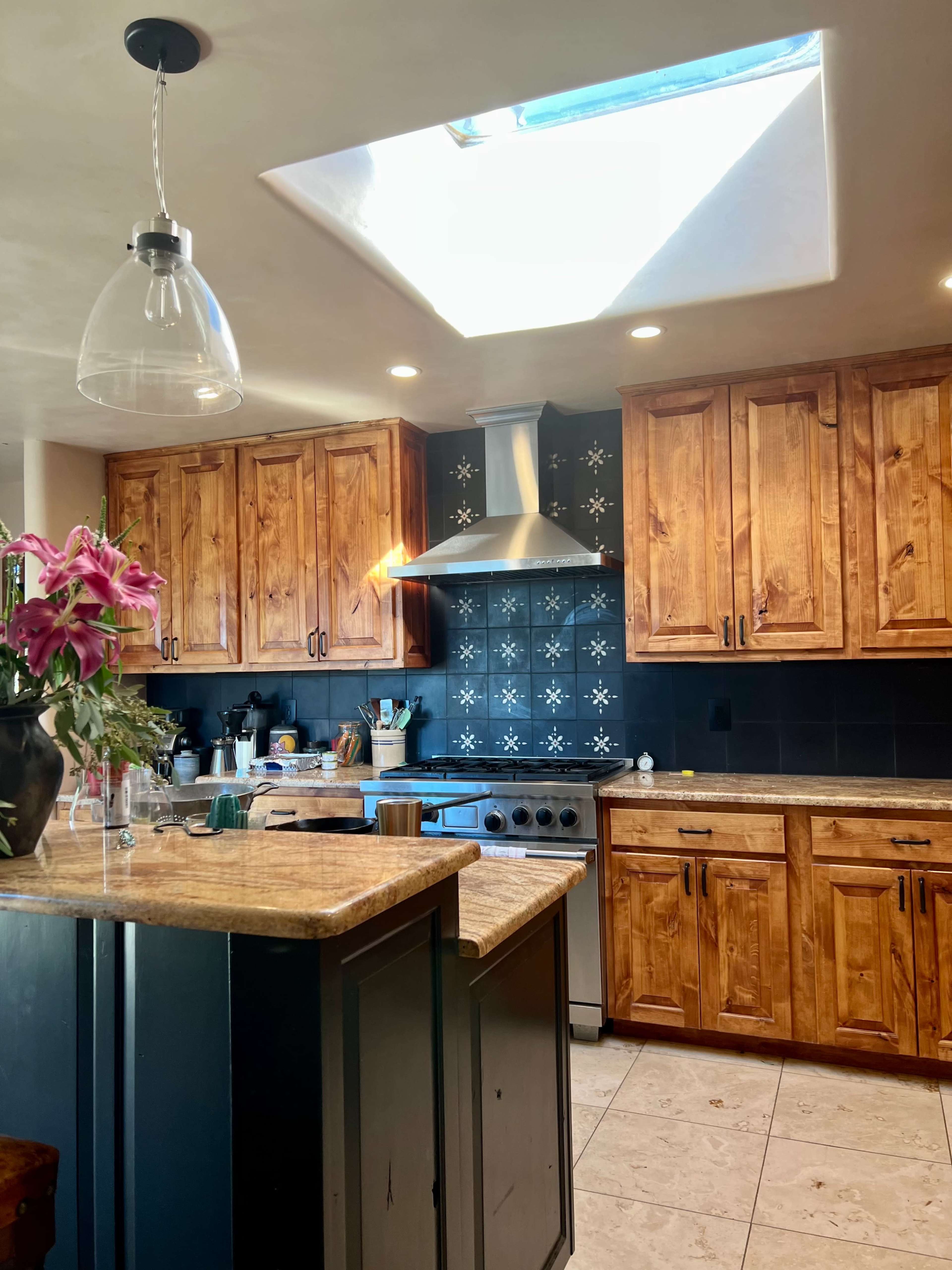 A modern kitchen features wooden cabinets, a stainless steel range hood, and a skylight illuminating the space.