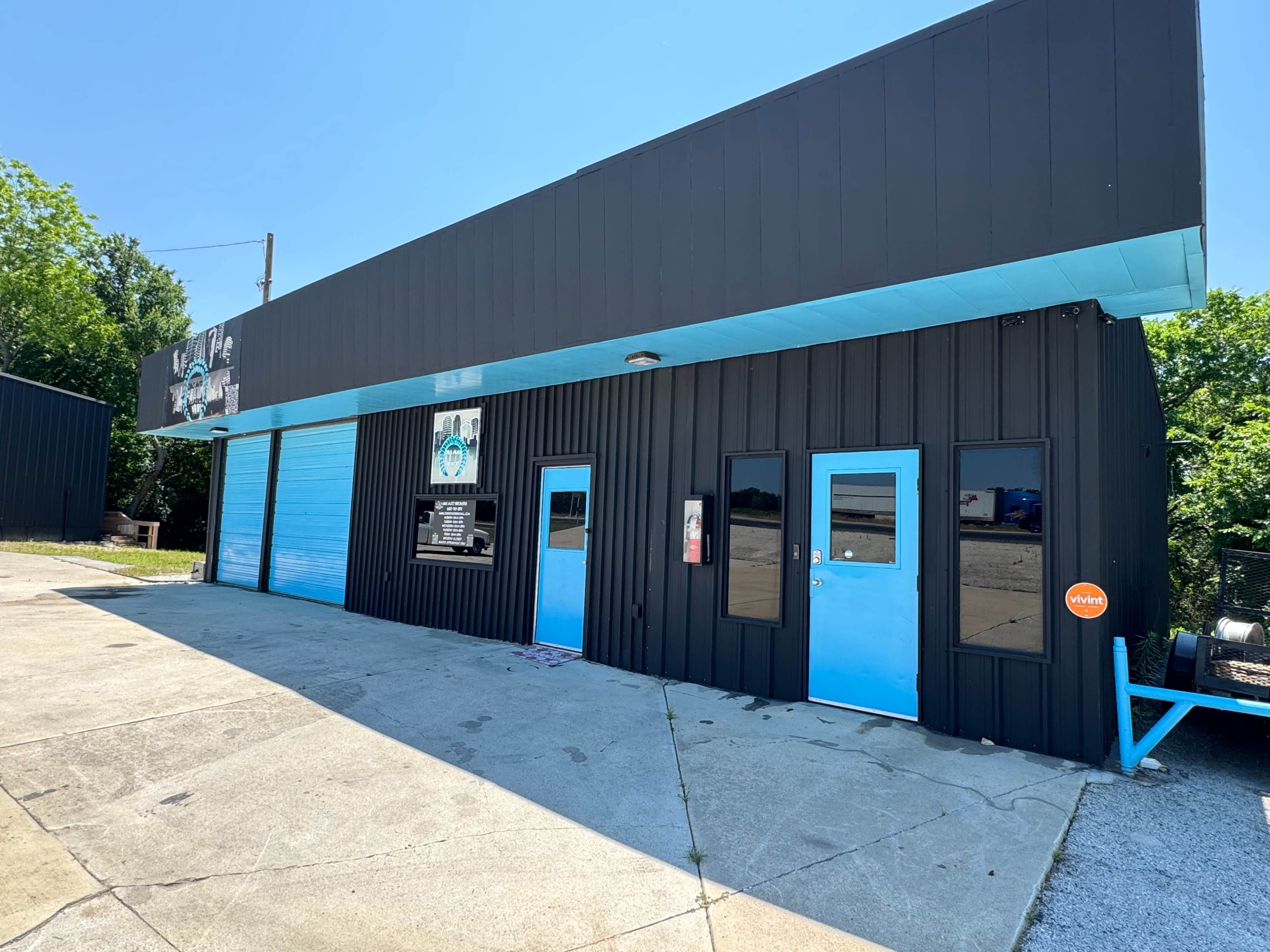 The image shows a black and blue commercial building with large windows and a roll-up garage door.