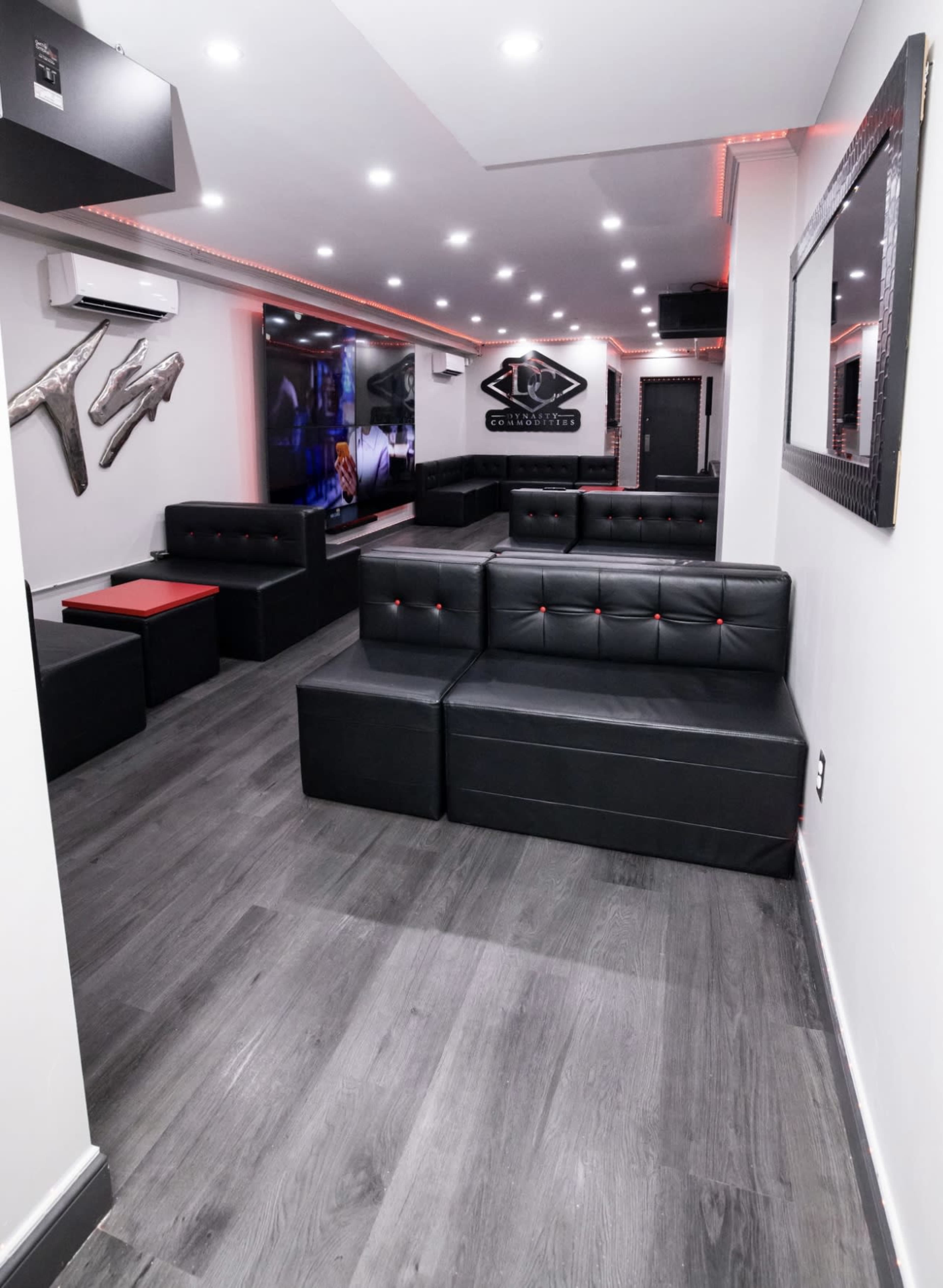 The image shows a modern lounge with black seating, a large screen on the wall, and red accent lighting.