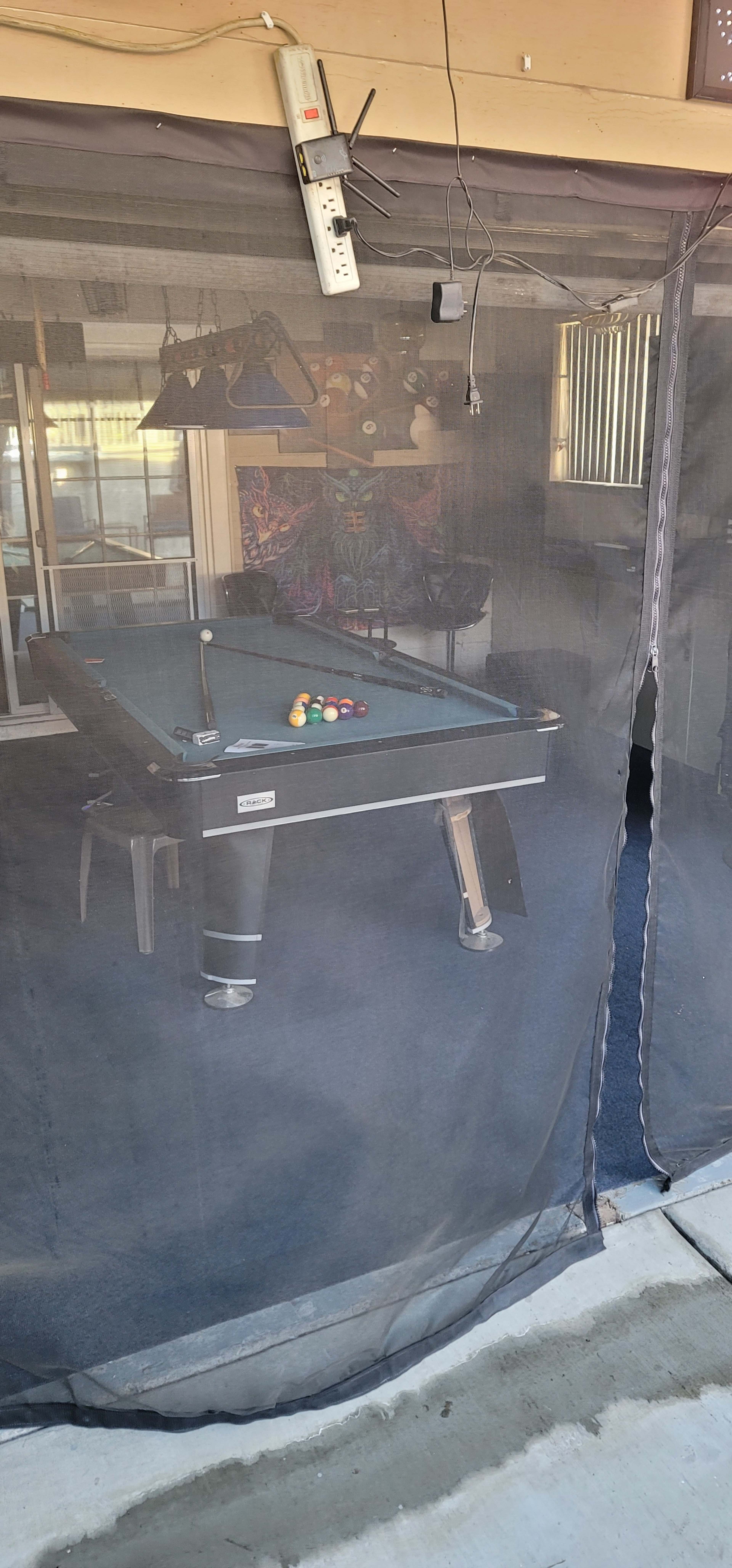 A pool table is visible through a mesh curtain in a shaded room.
