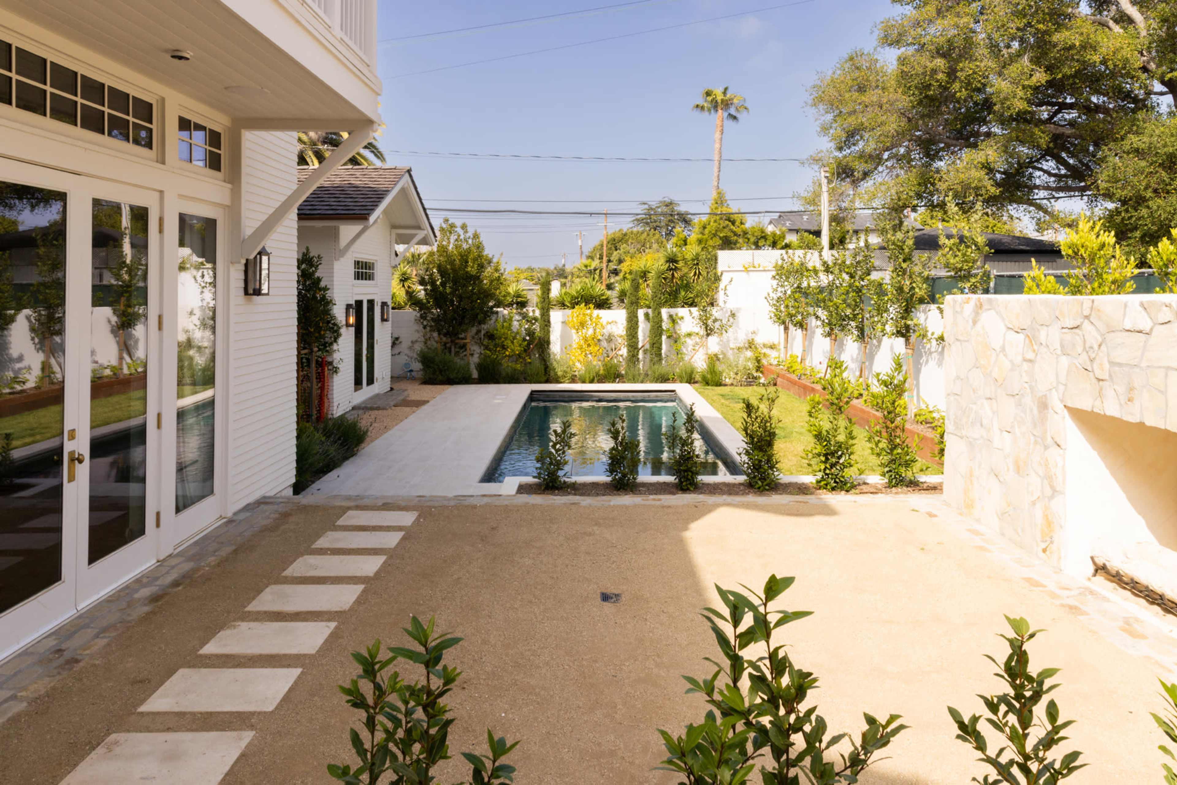A backyard with a small pool bordered by grassy areas and landscaped gardens, alongside a modern house.