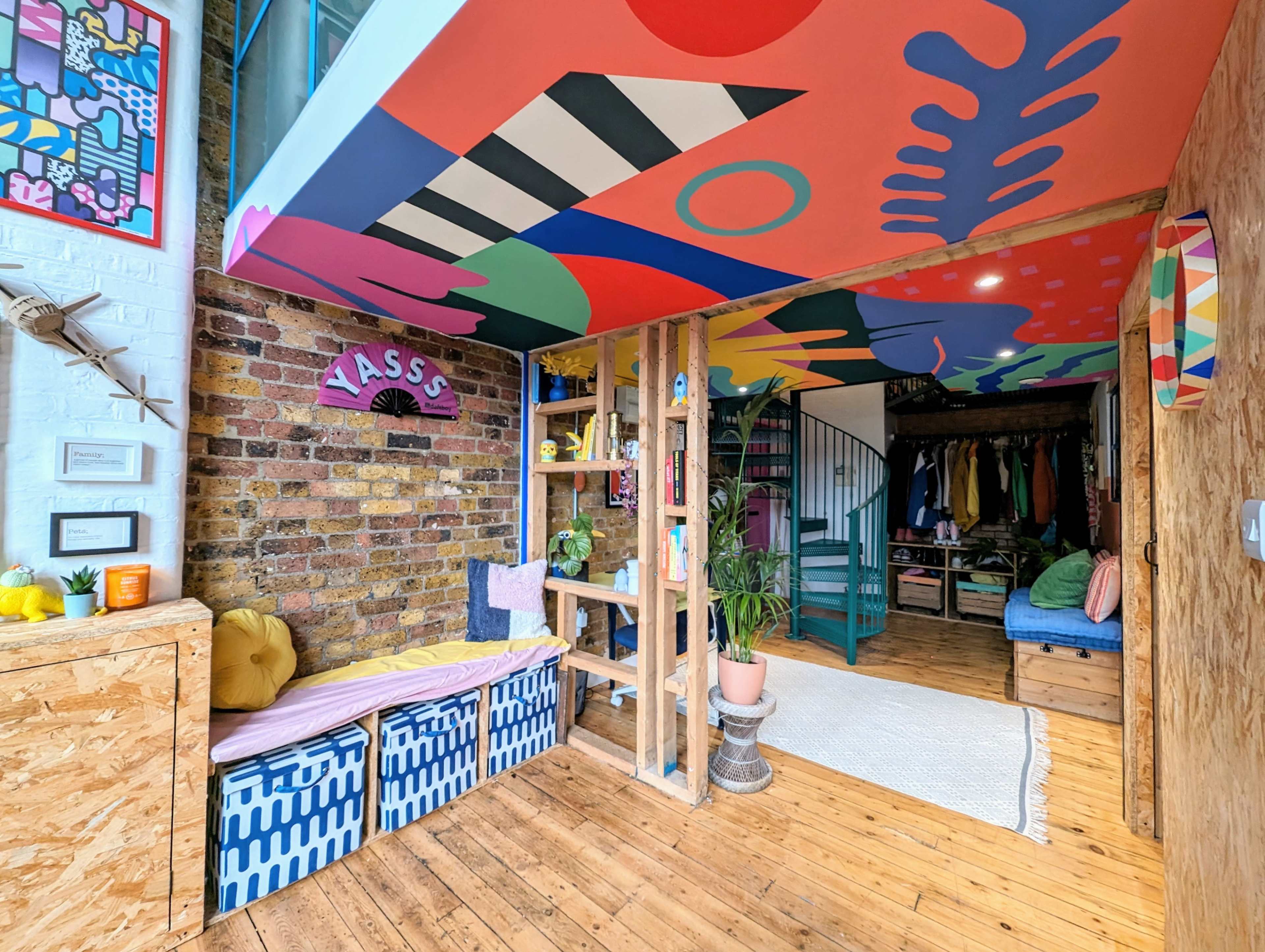 A colorful, modern living space with a spiral staircase, a cozy seating area, and a closet filled with various clothing items.