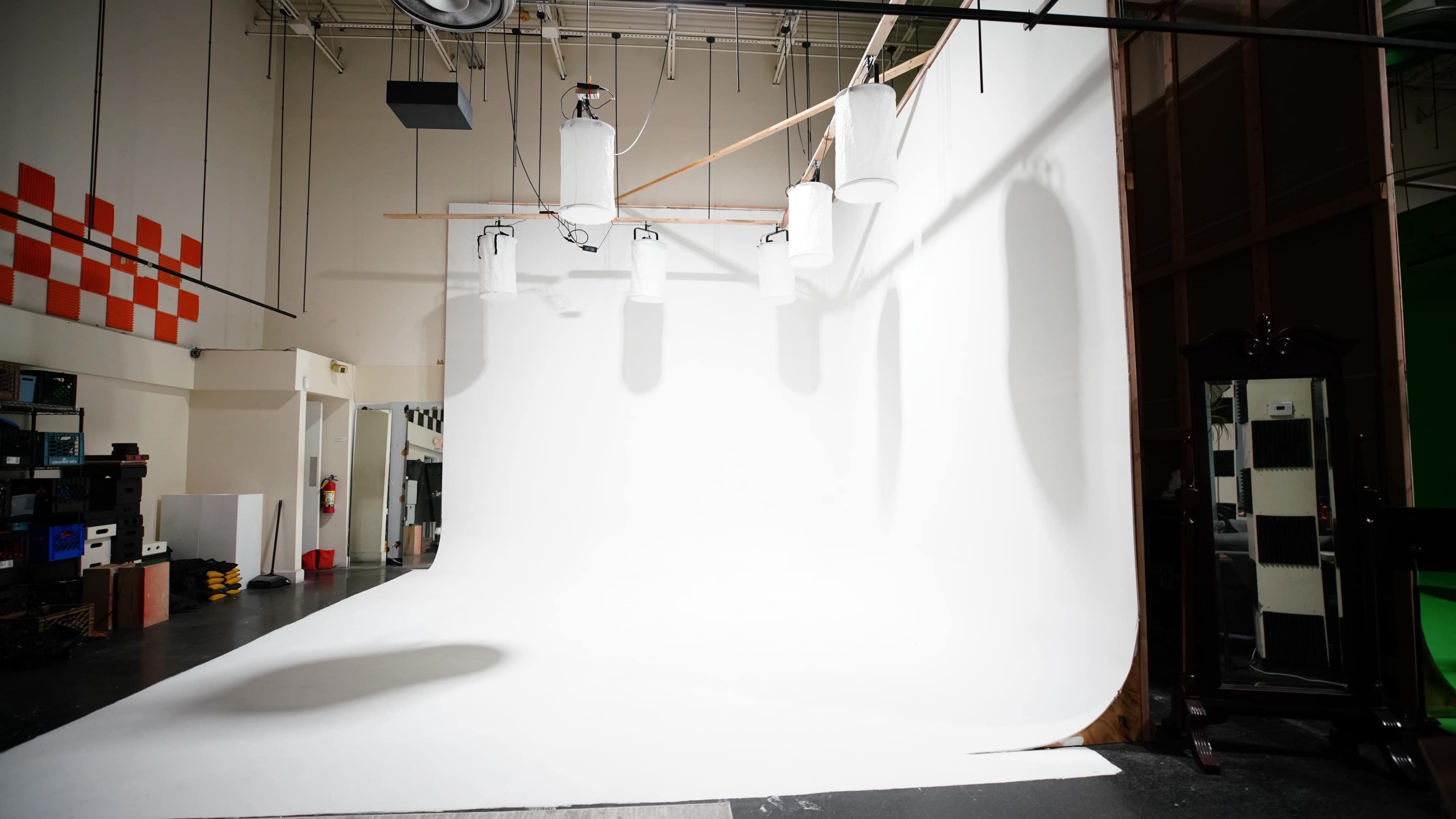 A photography studio featuring a seamless white backdrop, overhead lighting, and various equipment along the walls.