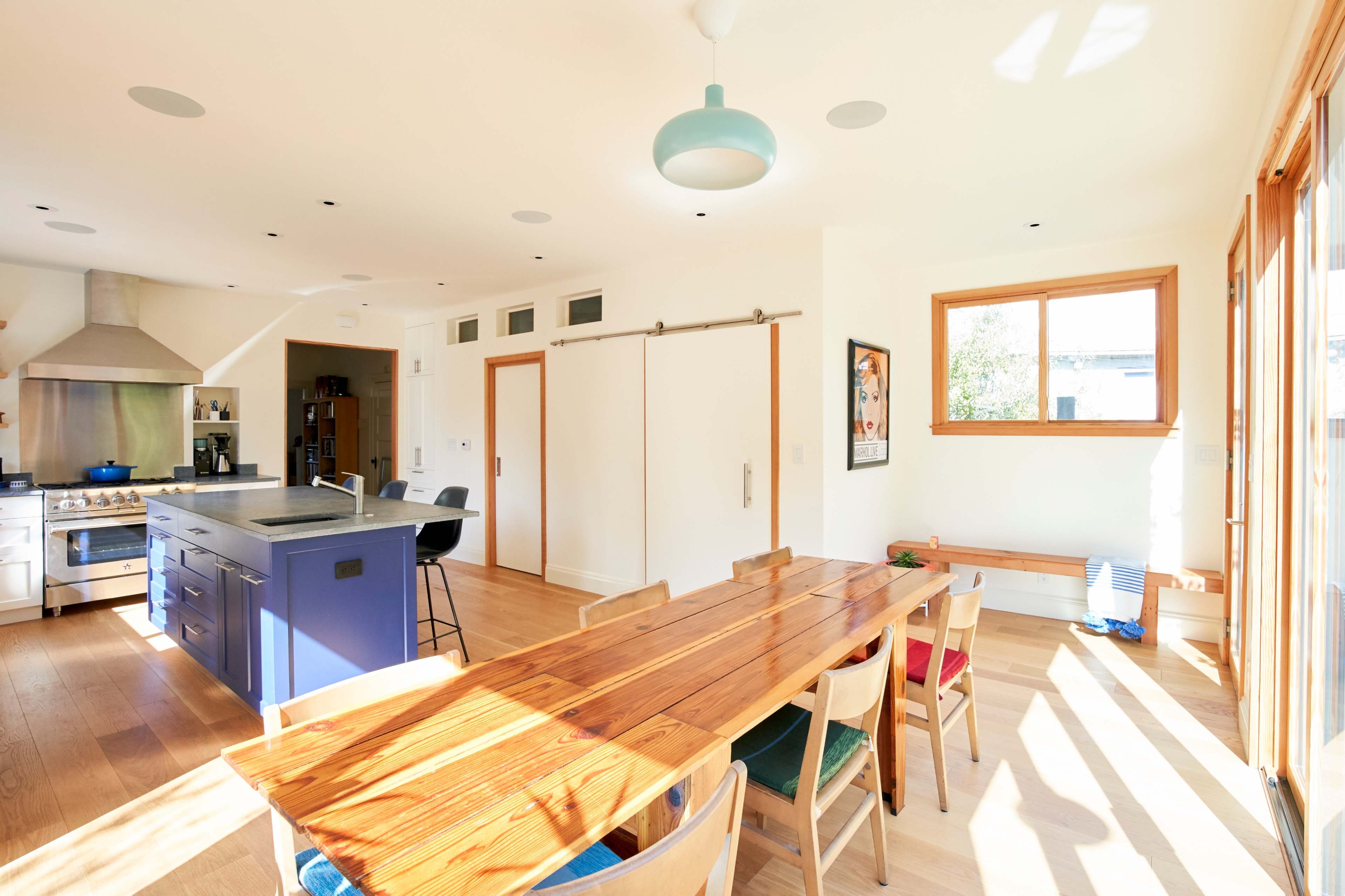 A spacious kitchen and dining area features a large wooden table, an island with bar seating, and large windows allowing natural light to fill the room.