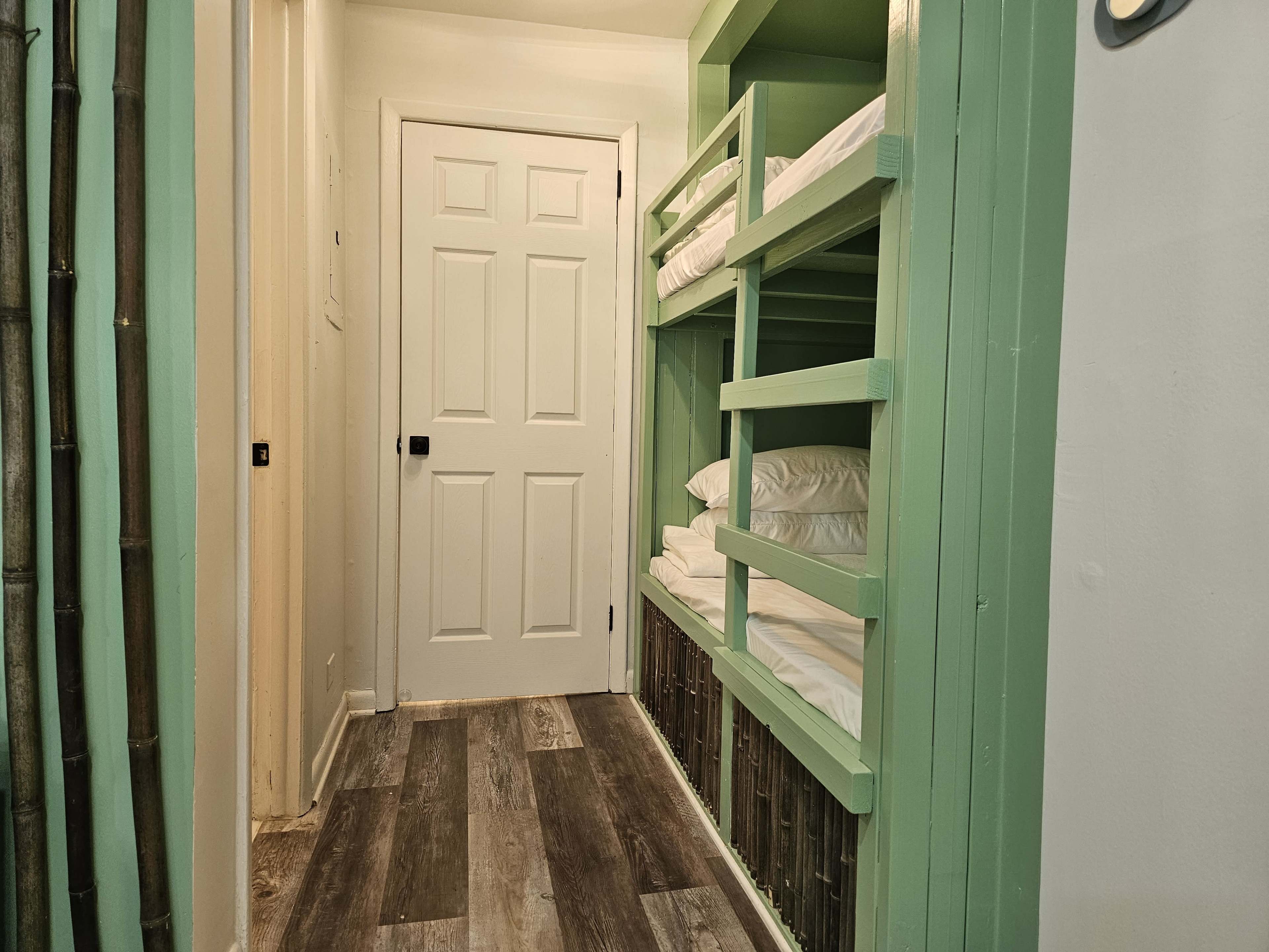 A narrow hallway features a closed white door and a set of green bunk beds against one wall.