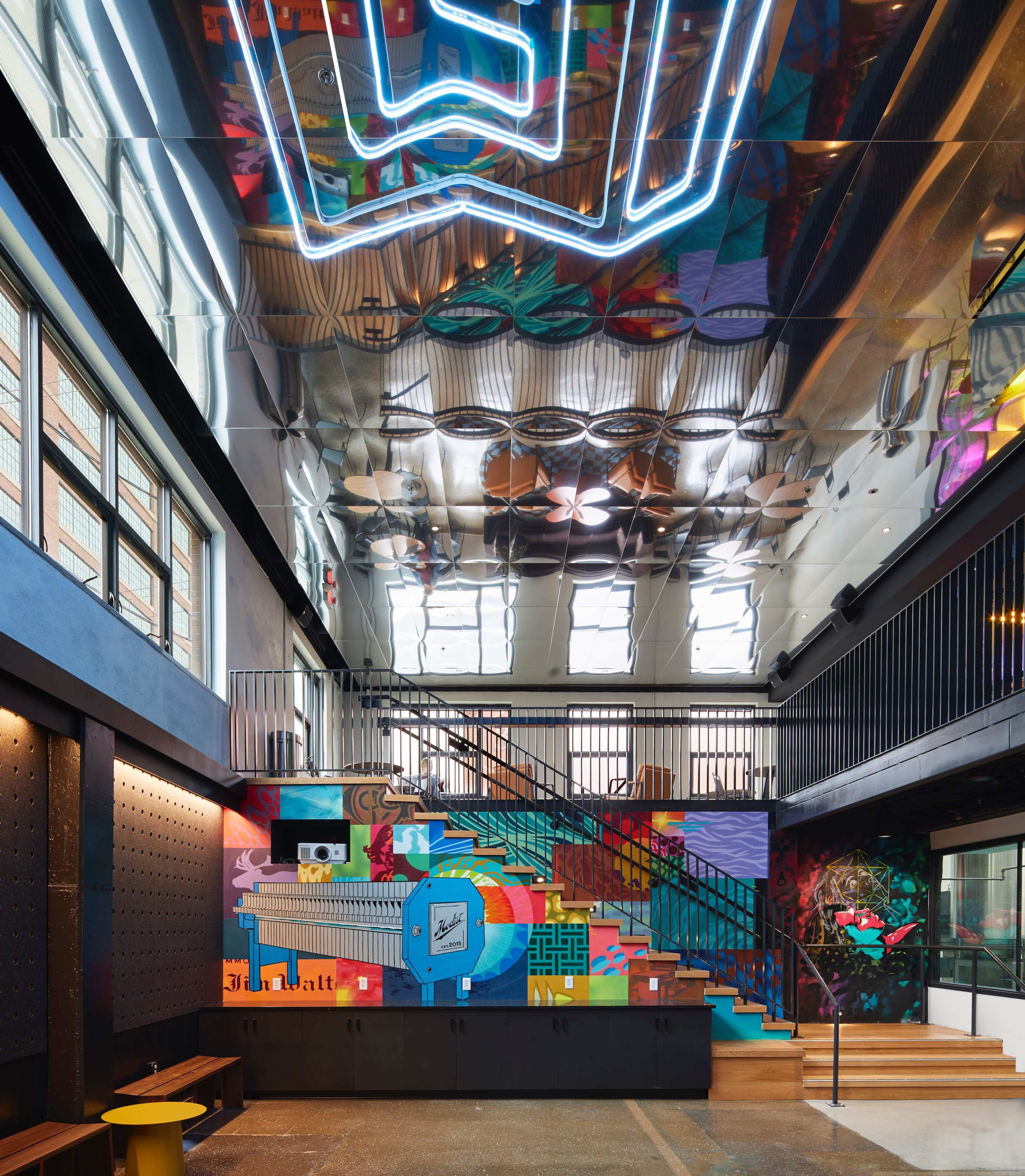 A vibrant interior space featuring a colorful mural, reflective ceiling, and a staircase leading to an upper level.