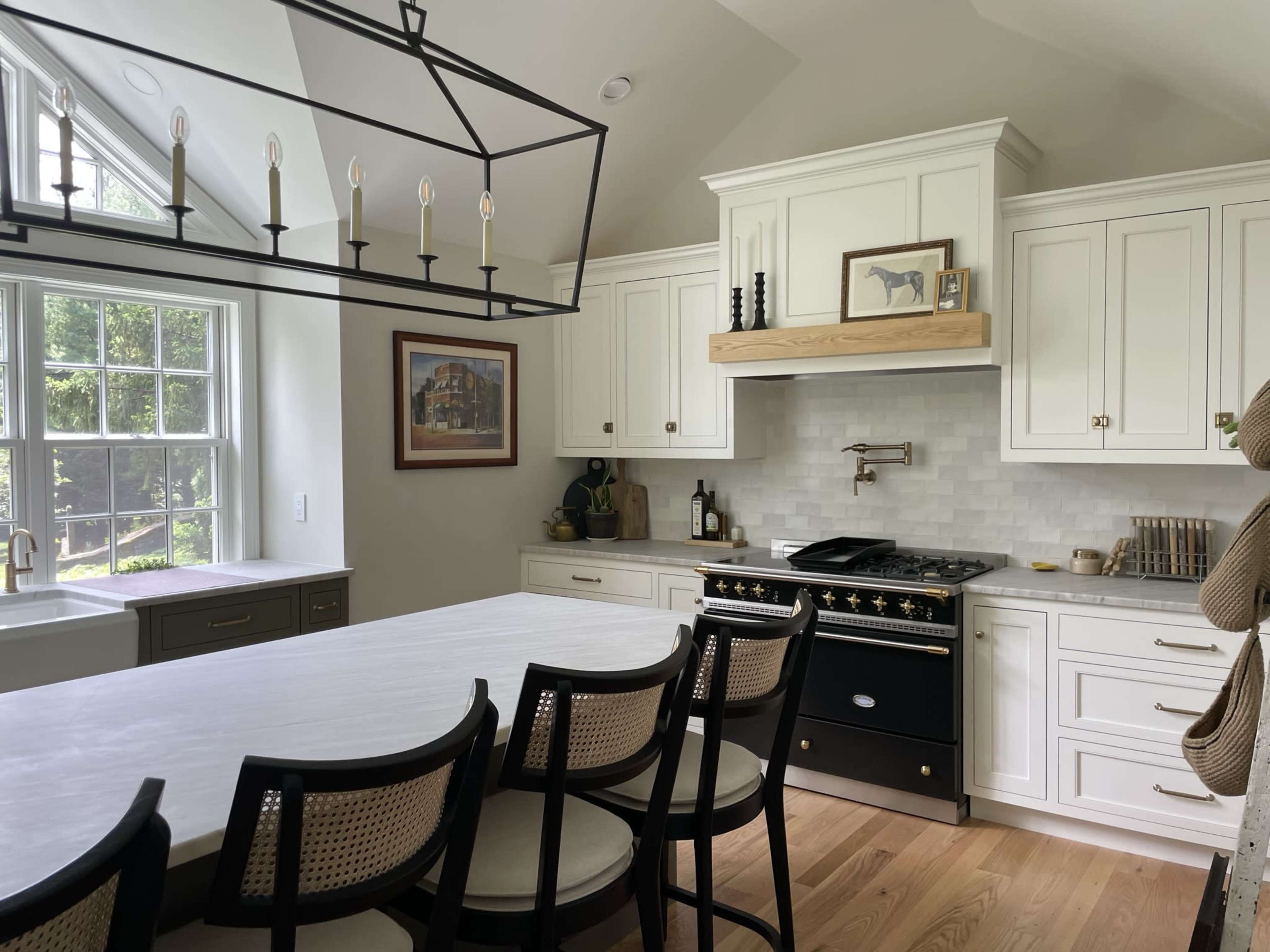 A modern kitchen features white cabinetry, a central island with seating, a black stove, and large windows allowing natural light.