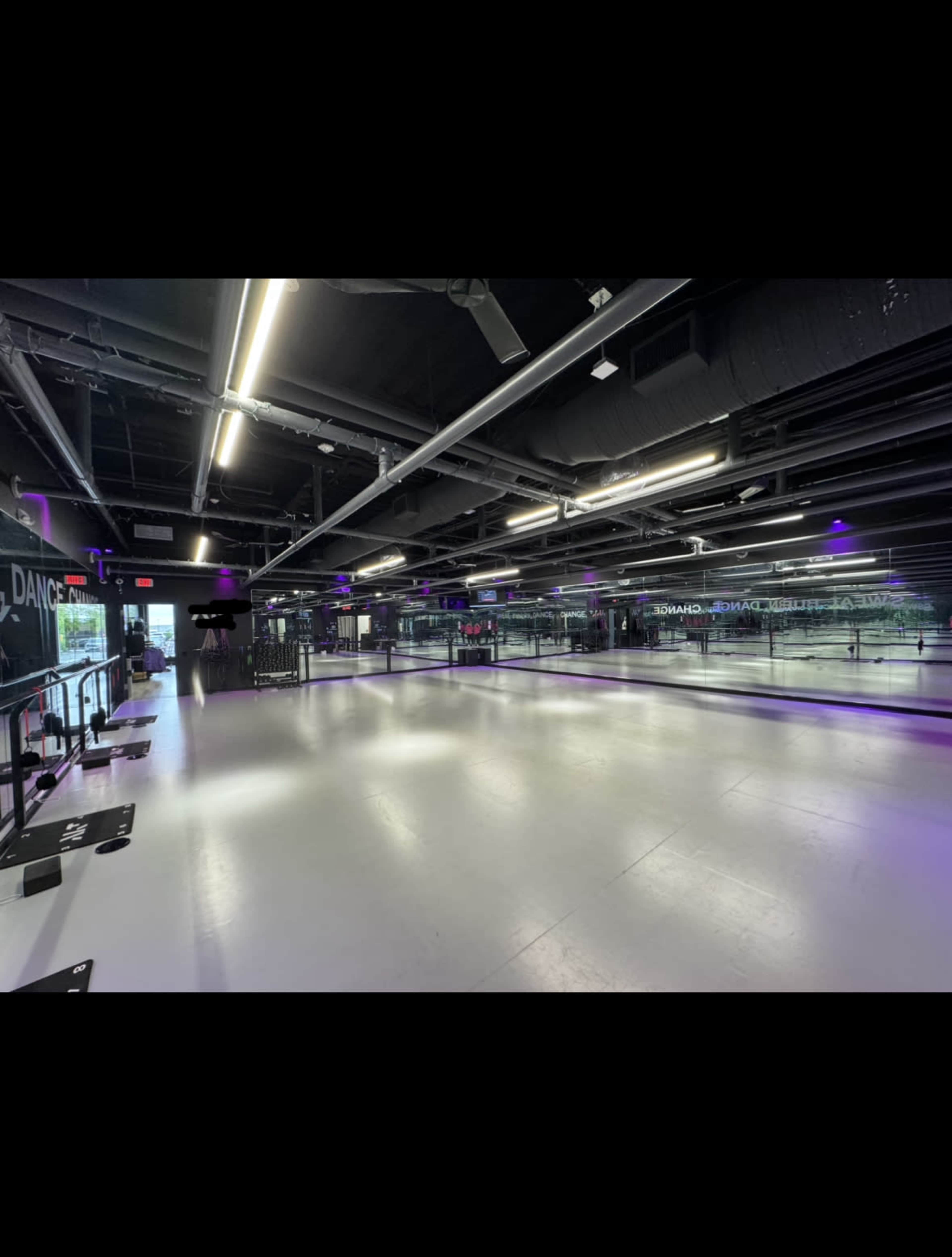 A spacious dance studio with mirrored walls, bright lighting, and a smooth floor.