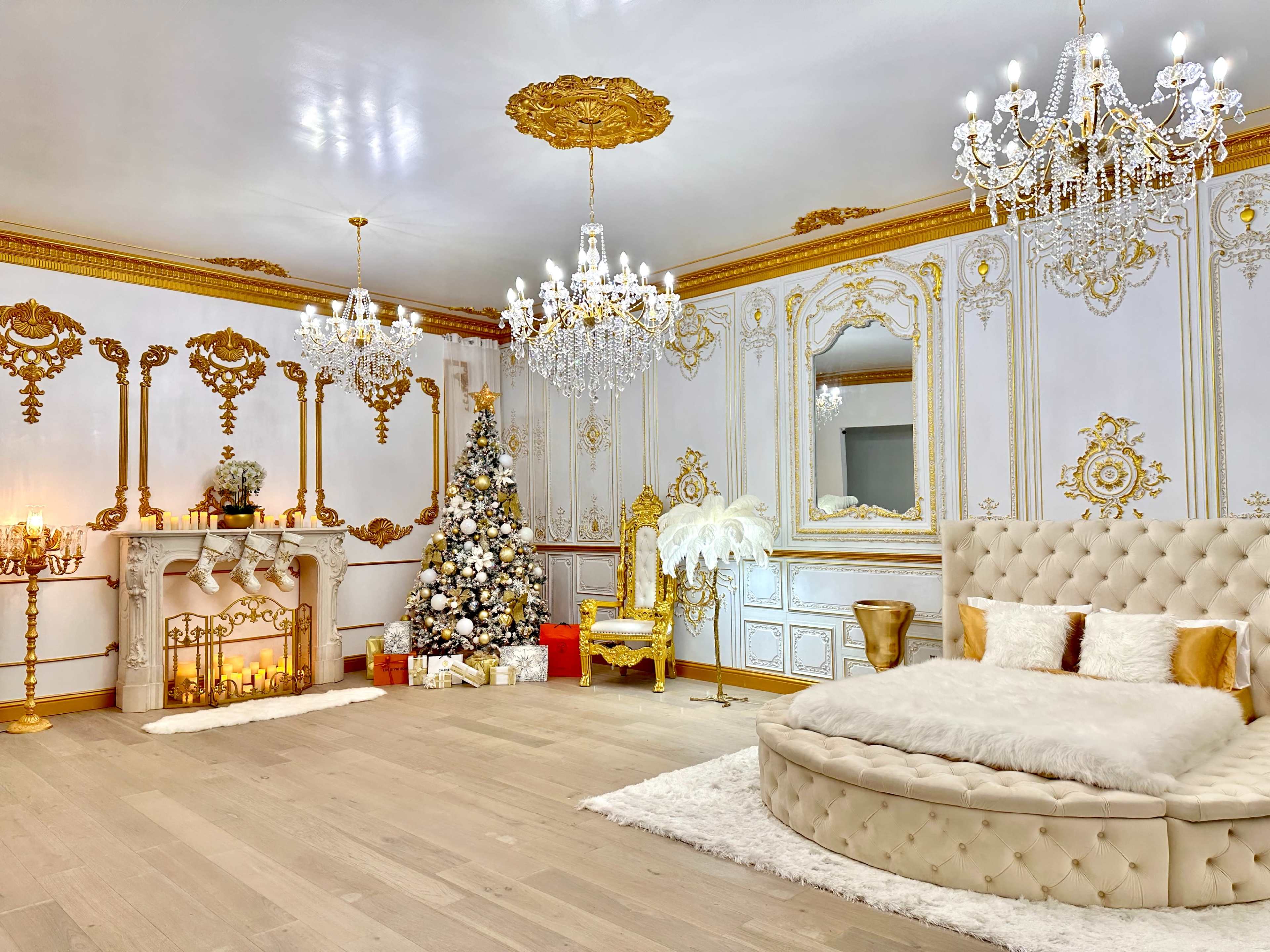 The image shows an elegantly decorated room featuring a plush round bed, a Christmas tree adorned with ornaments, and ornate chandeliers hanging from the ceiling.