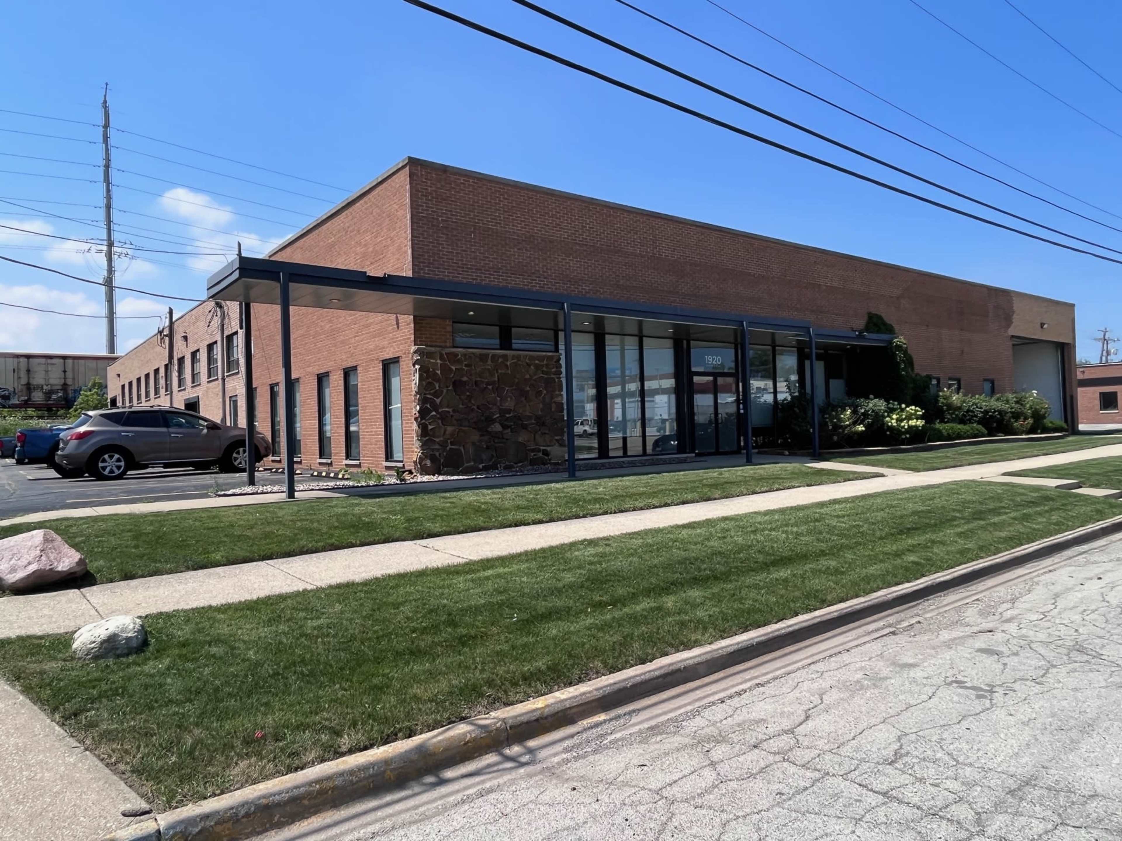 A single-story brick office building with large front windows and a landscaped area is located beside a paved parking lot.