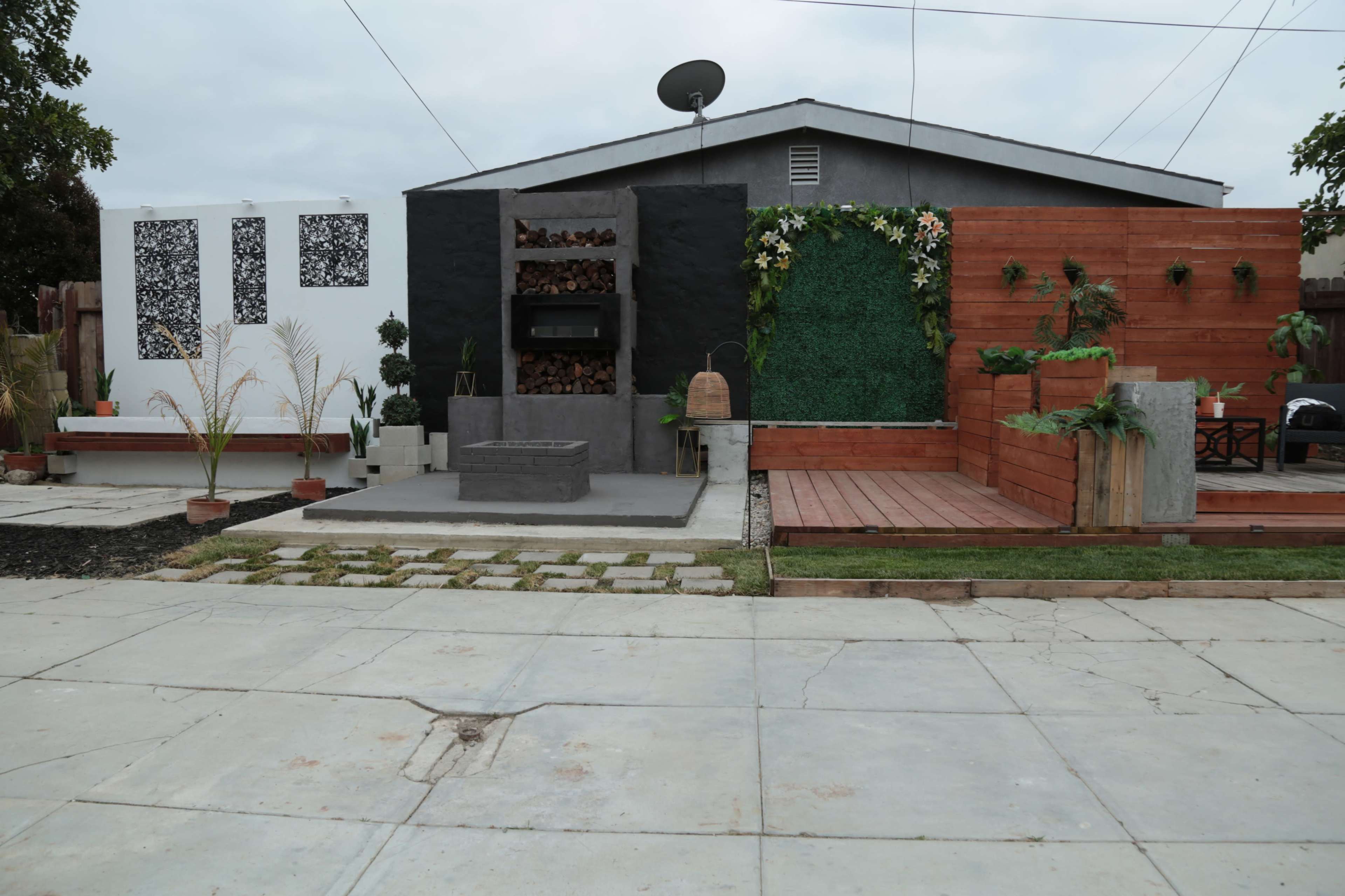 A modern outdoor space featuring a concrete seating area, a wall with decorative designs, and landscaping elements, including planters and wooden decking.