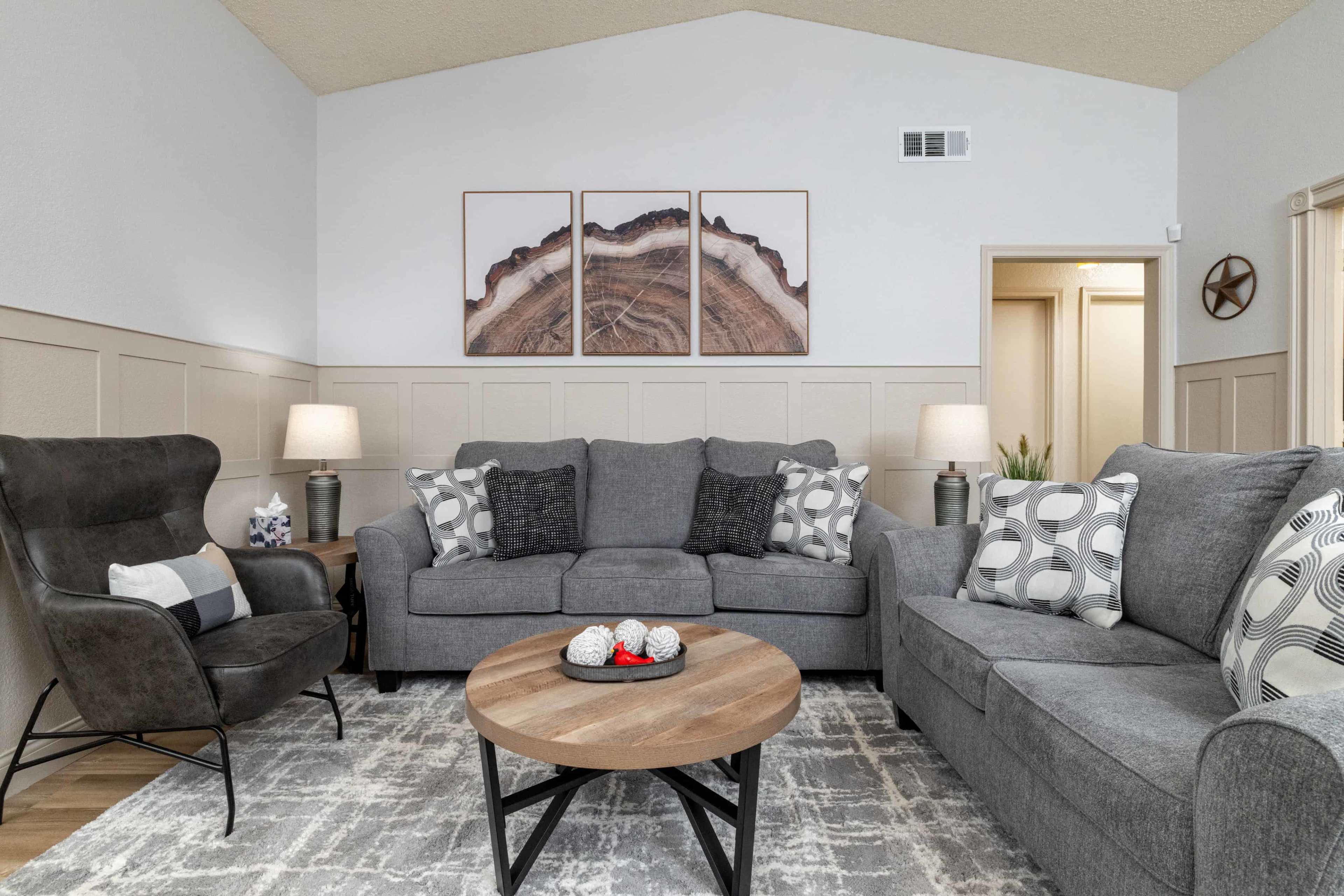 A cozy living room features a sectional sofa, two armchairs, decorative pillows, and a coffee table, with wall art mounted above the sofa.