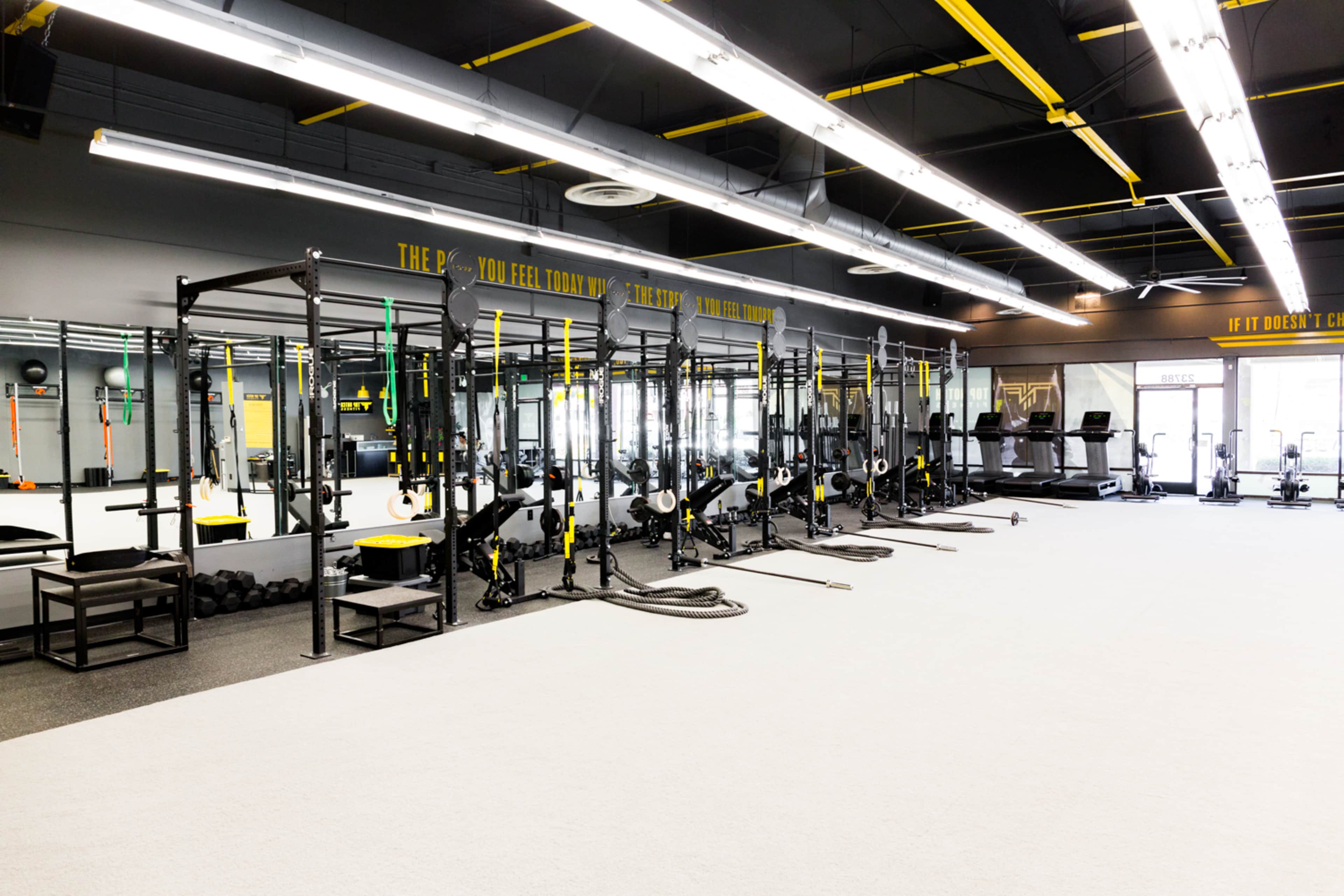 A well-equipped gym interior featuring multiple workout stations, including squat racks and weightlifting benches, illuminated by overhead lights.
