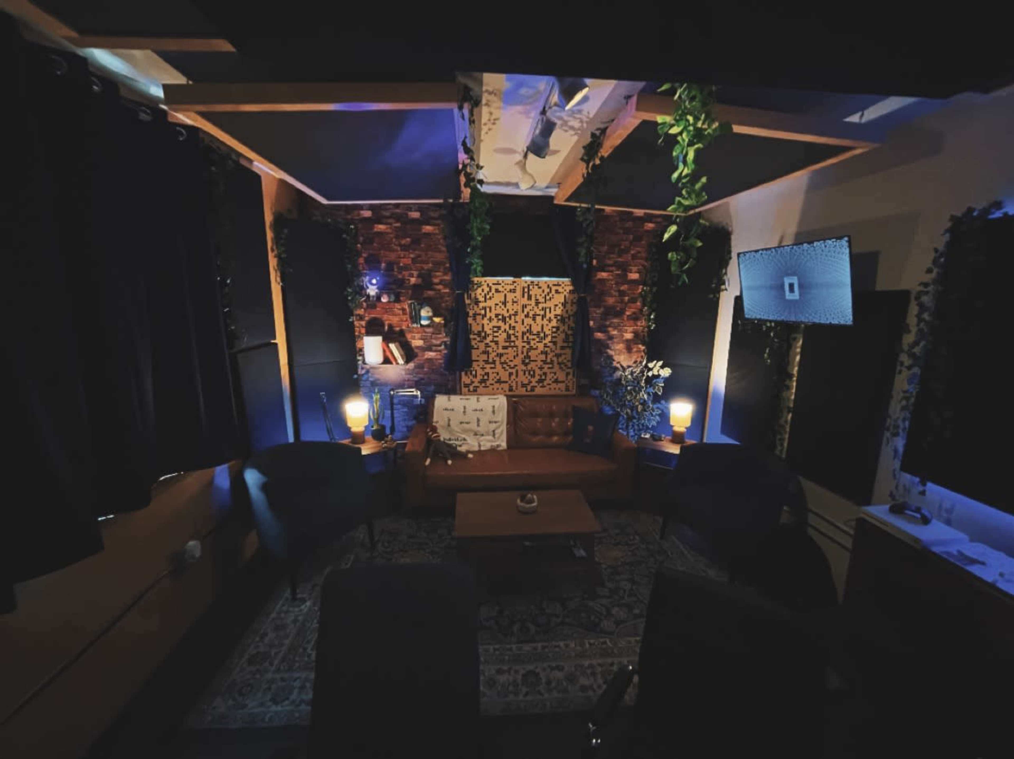 A cozy lounge area features a brown leather sofa, a wooden coffee table, and dim lighting, surrounded by dark curtains and plants.