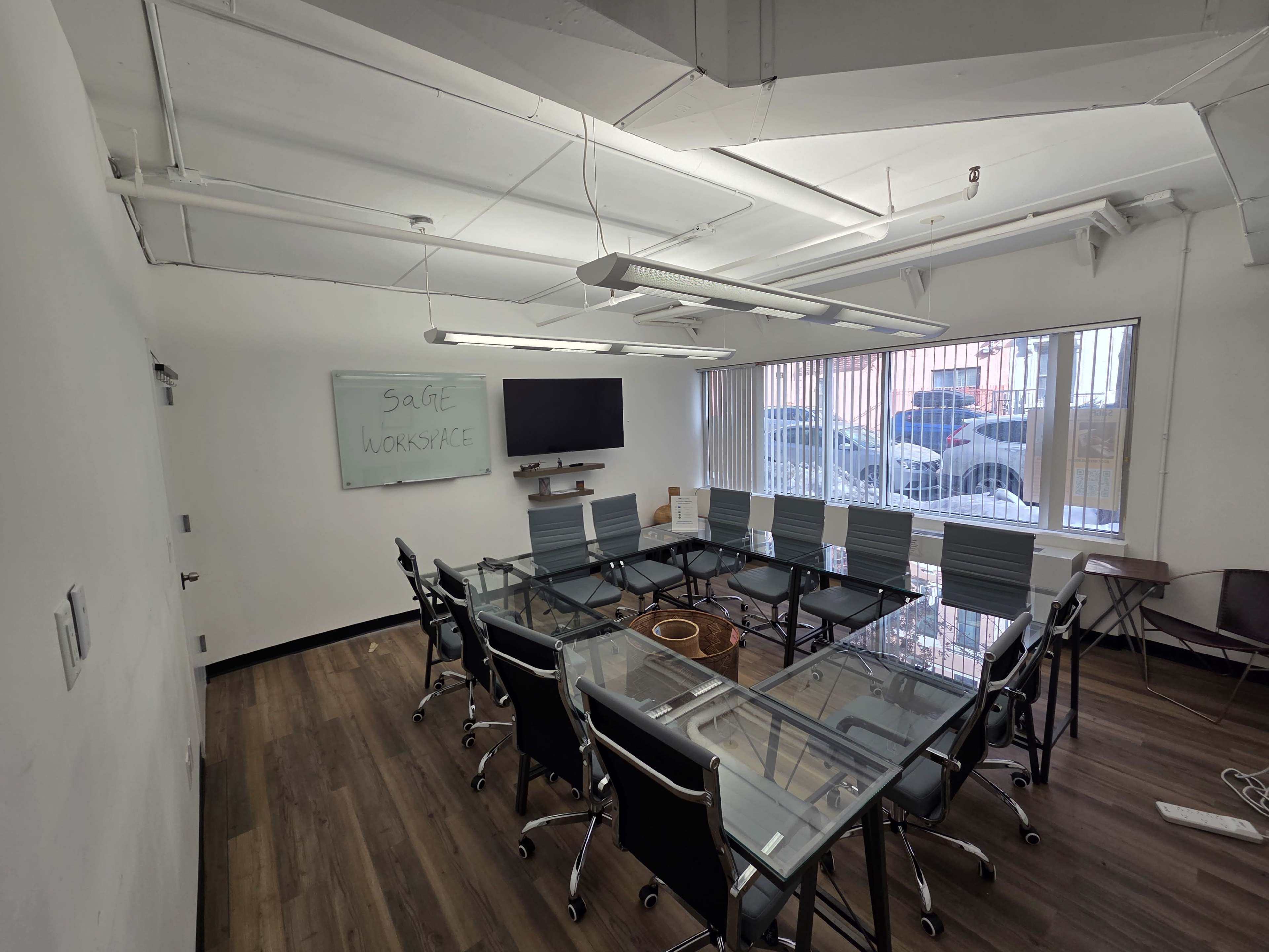 A modern conference room features a large glass table surrounded by black chairs, with a whiteboard and a television on the wall.