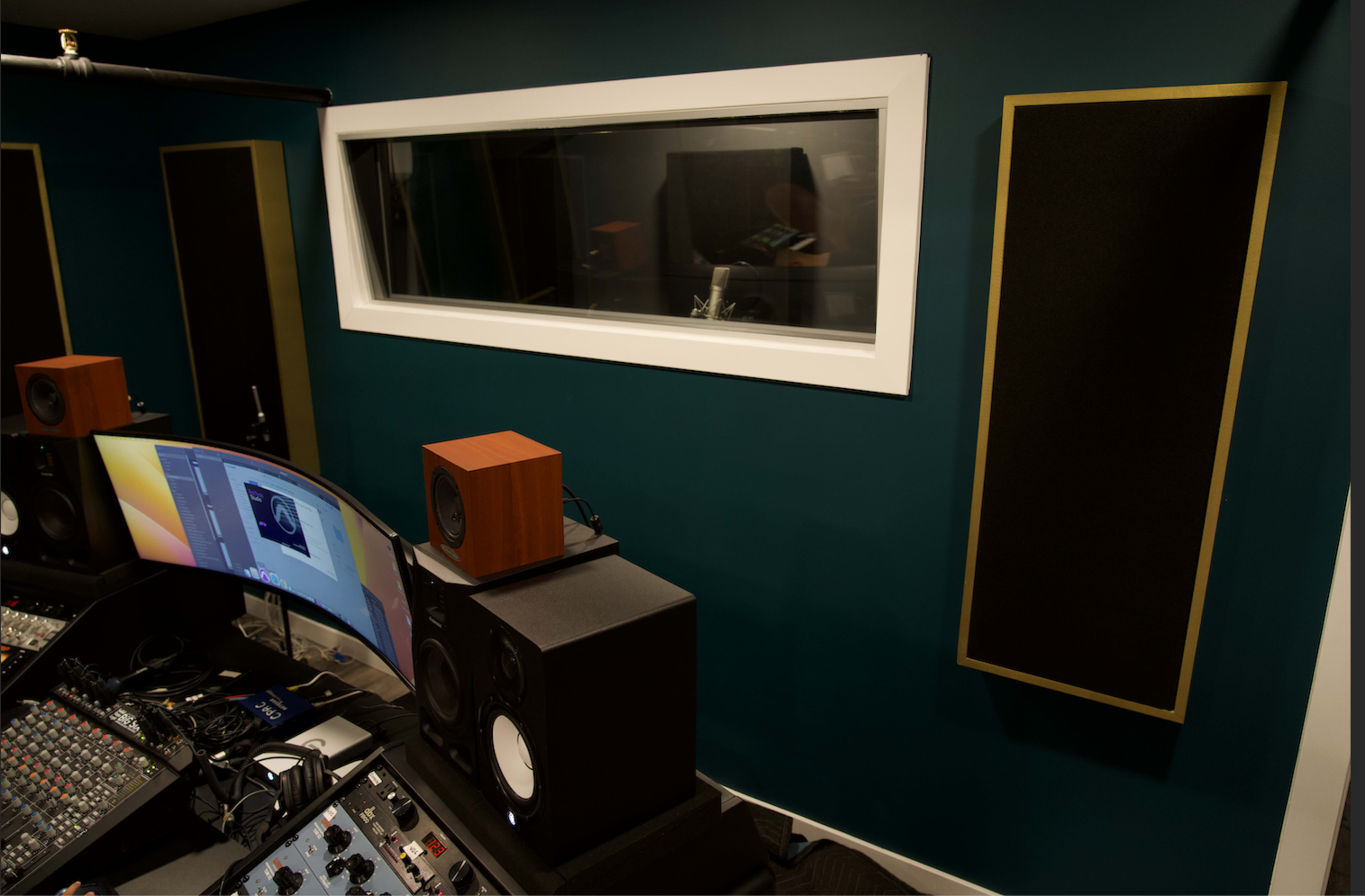A sound studio with a curved monitor, audio equipment, and soundproofing panels on the walls.