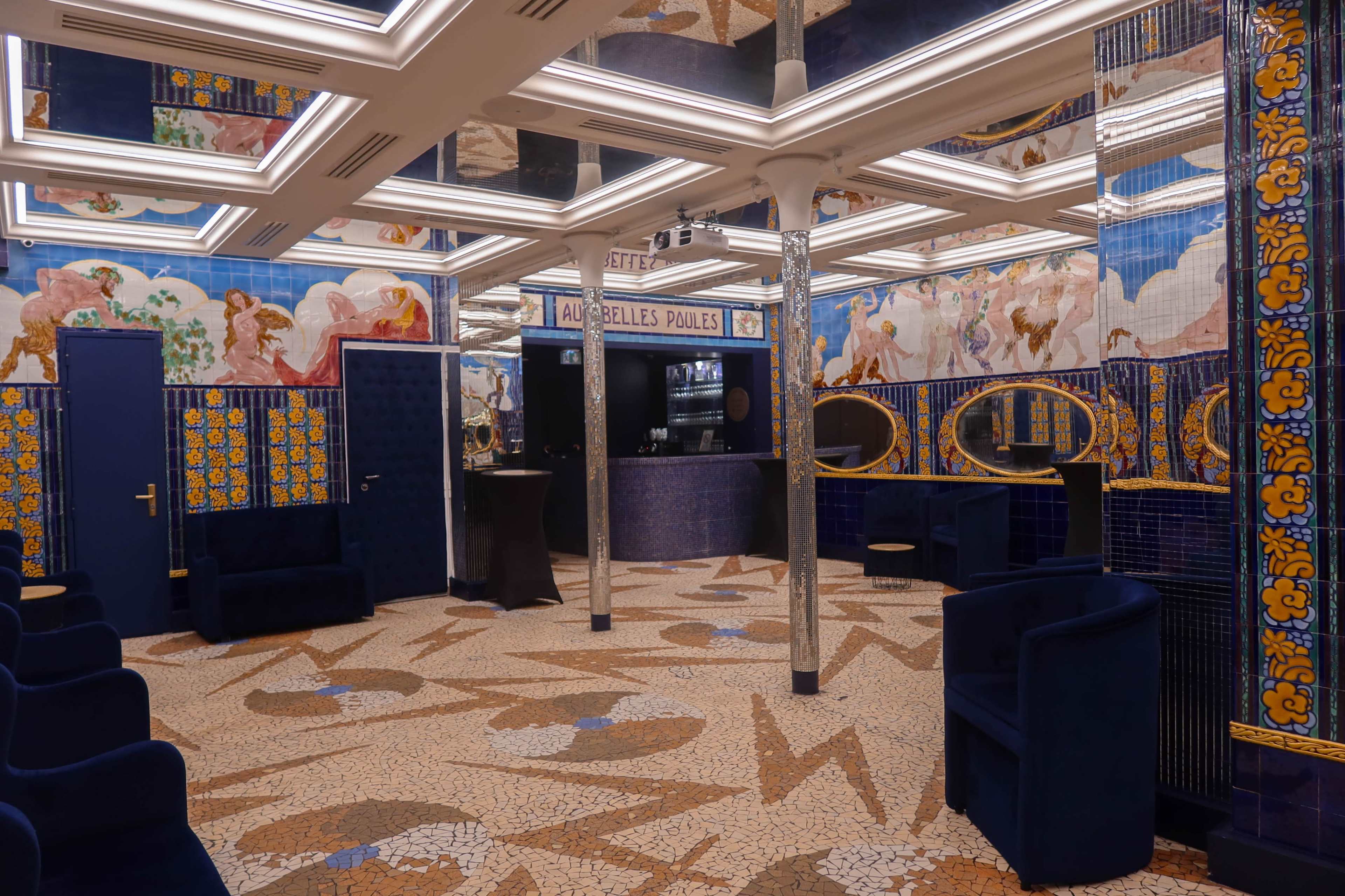 The image shows a brightly designed interior space featuring ornate blue and yellow tiles, mosaic flooring, and art-deco style decorations on the walls and ceiling.