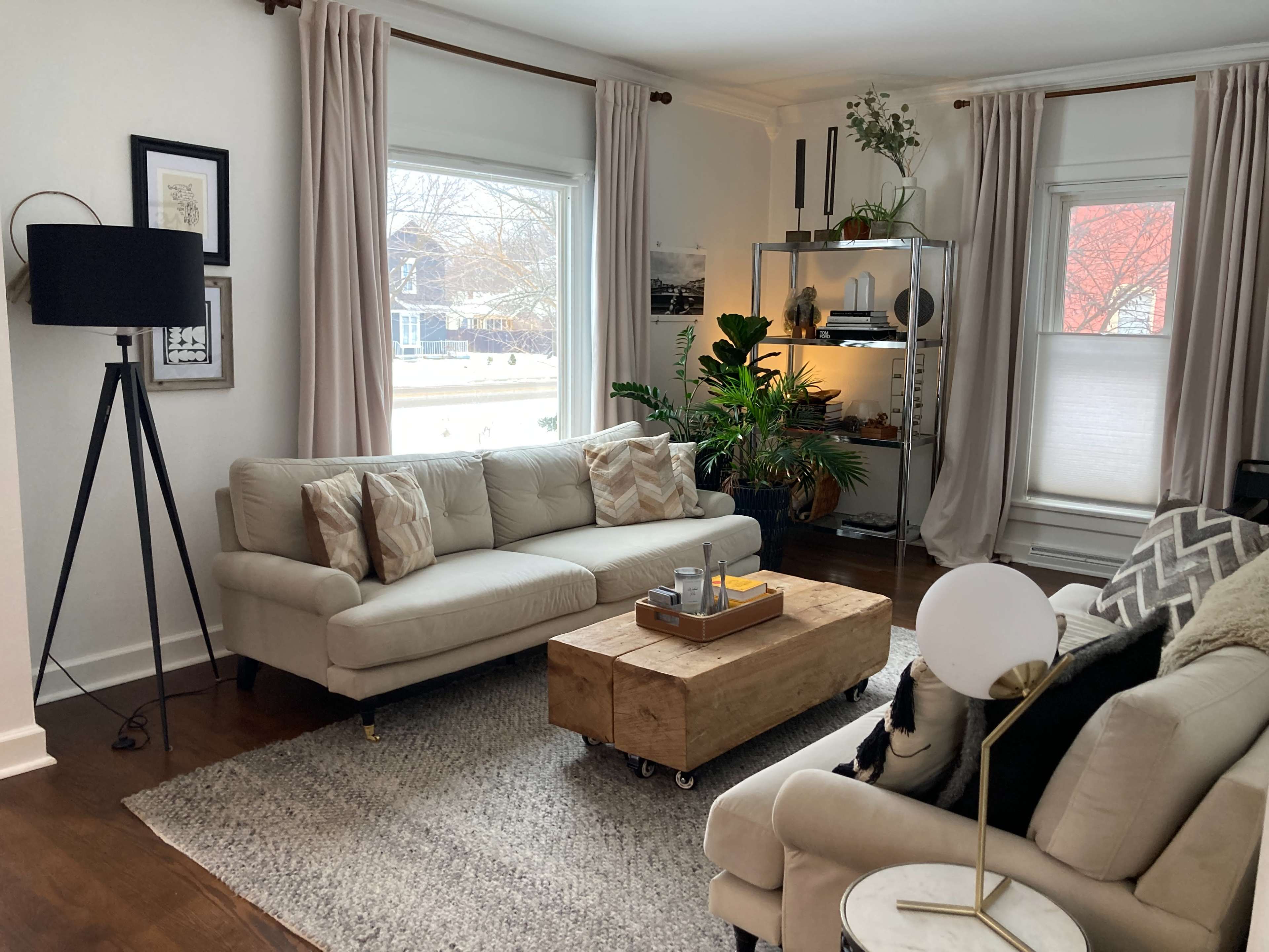 A living room with a light-colored sofa and a coffee table made from wood, surrounded by plants and modern decor.