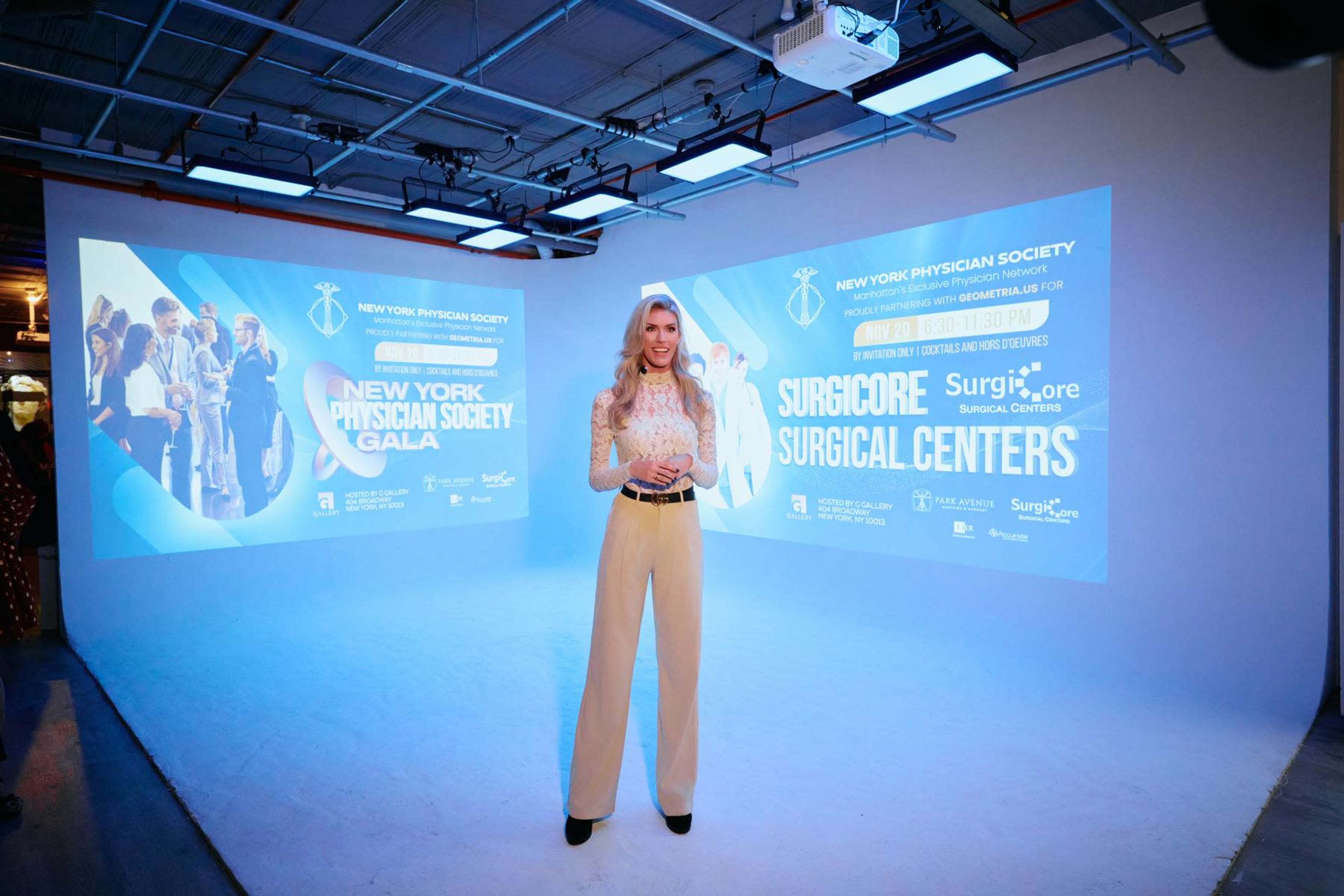 A woman stands in front of two large screens displaying promotional material for the New York Physician Society Gala and Surgicore Surgical Centers.