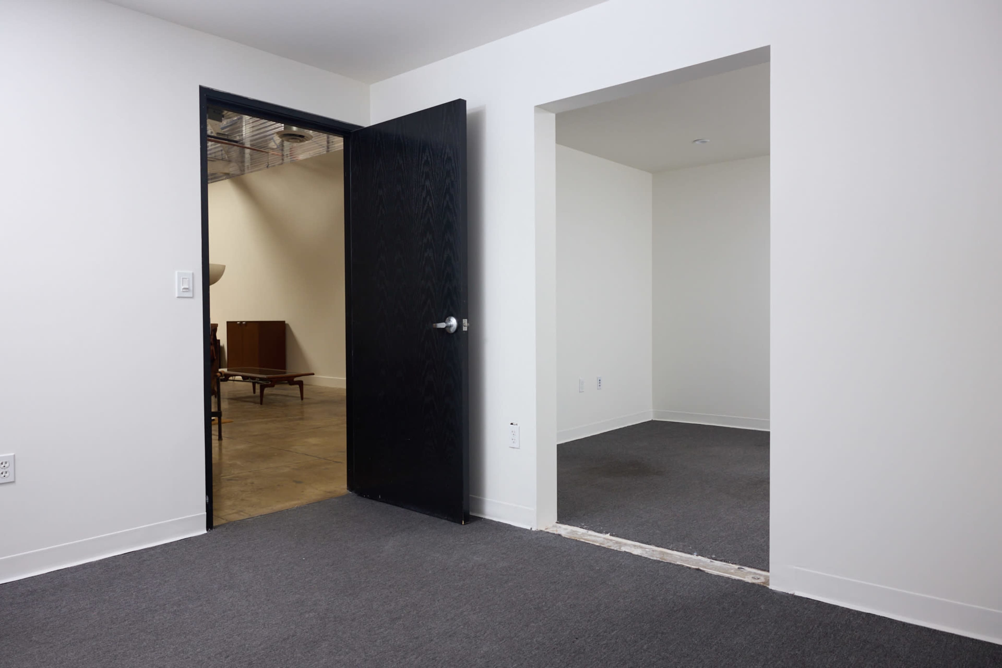 The image shows a minimalist interior of a room with an open doorway leading to another area and a cut-out section in the wall.