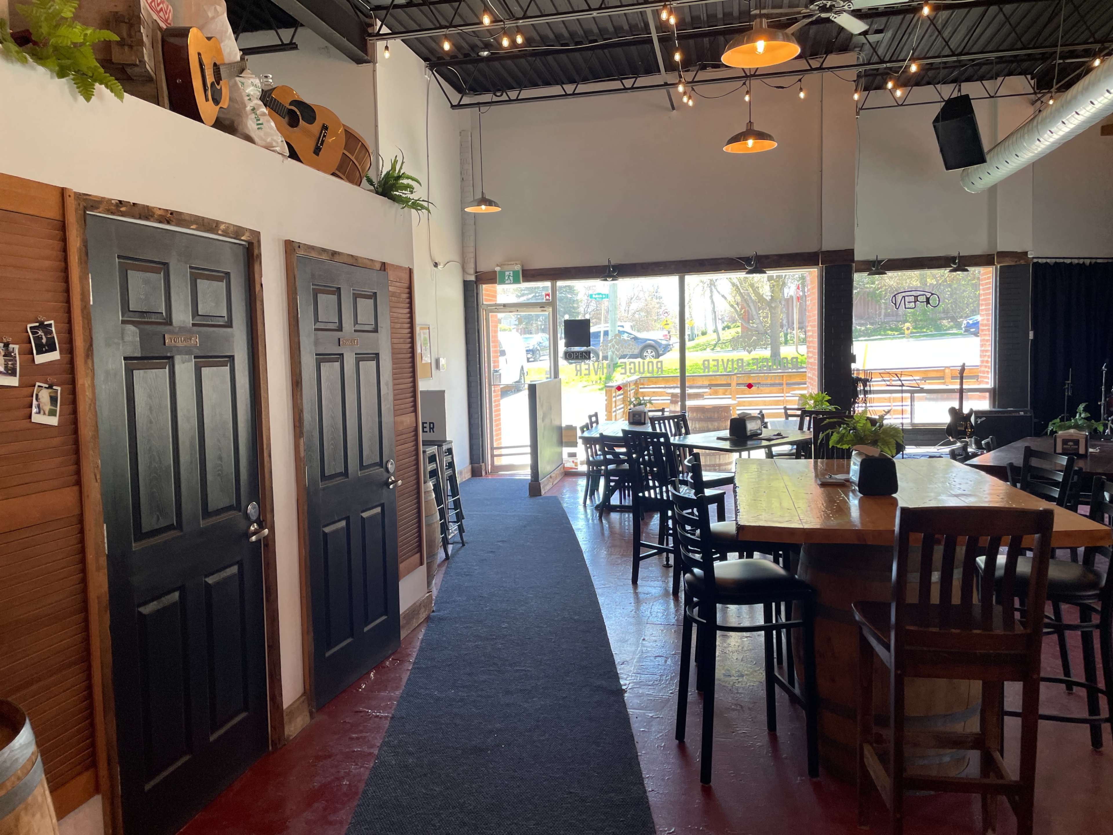 The interior of a restaurant or café with a path leading to two black doors on the left and a wooden table with chairs in the foreground.