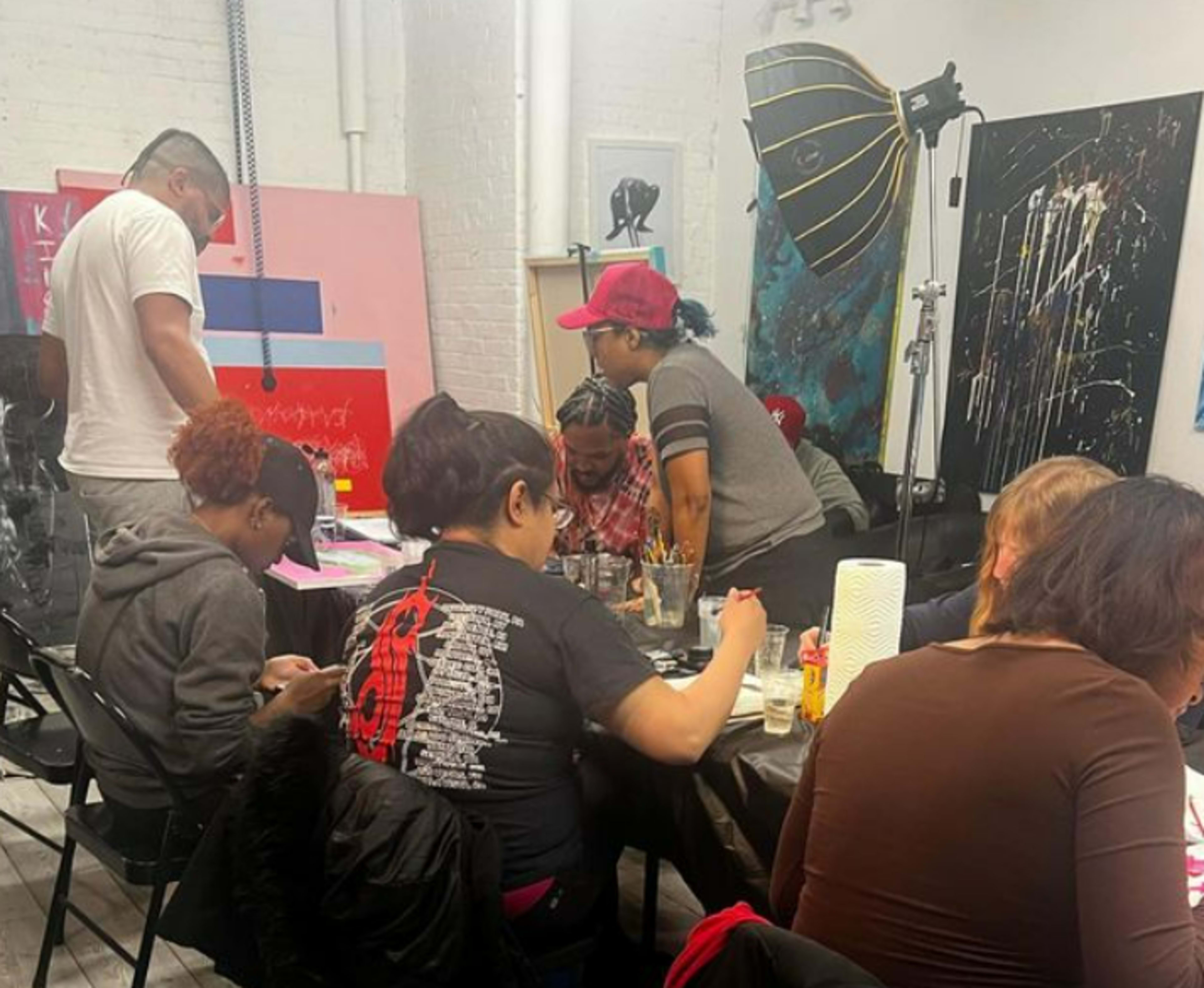 A group of people is gathered around tables in an art studio, engaged in a painting activity.