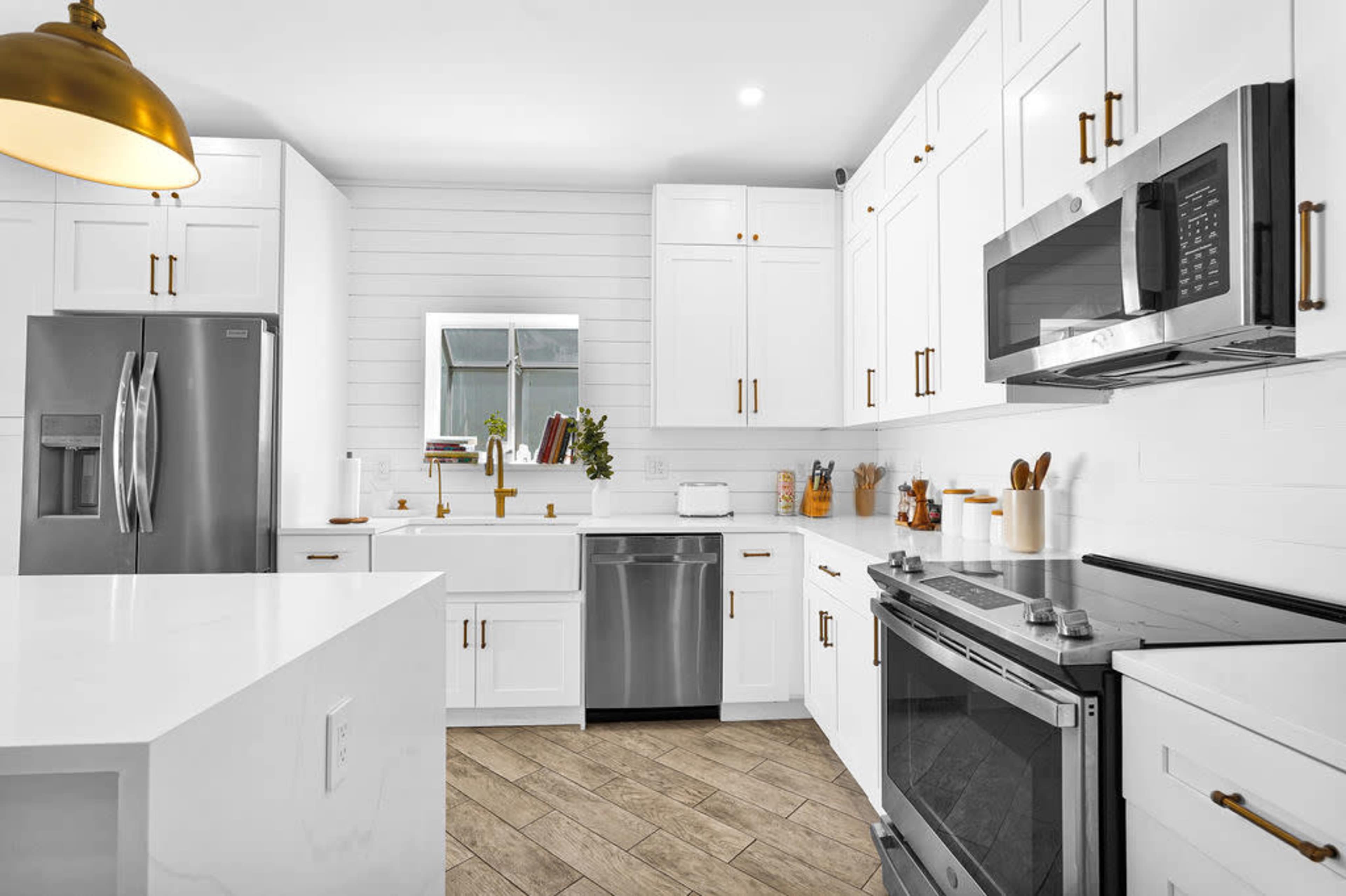 The kitchen features white cabinetry, stainless steel appliances, and a large island counter with a gold pendant light.