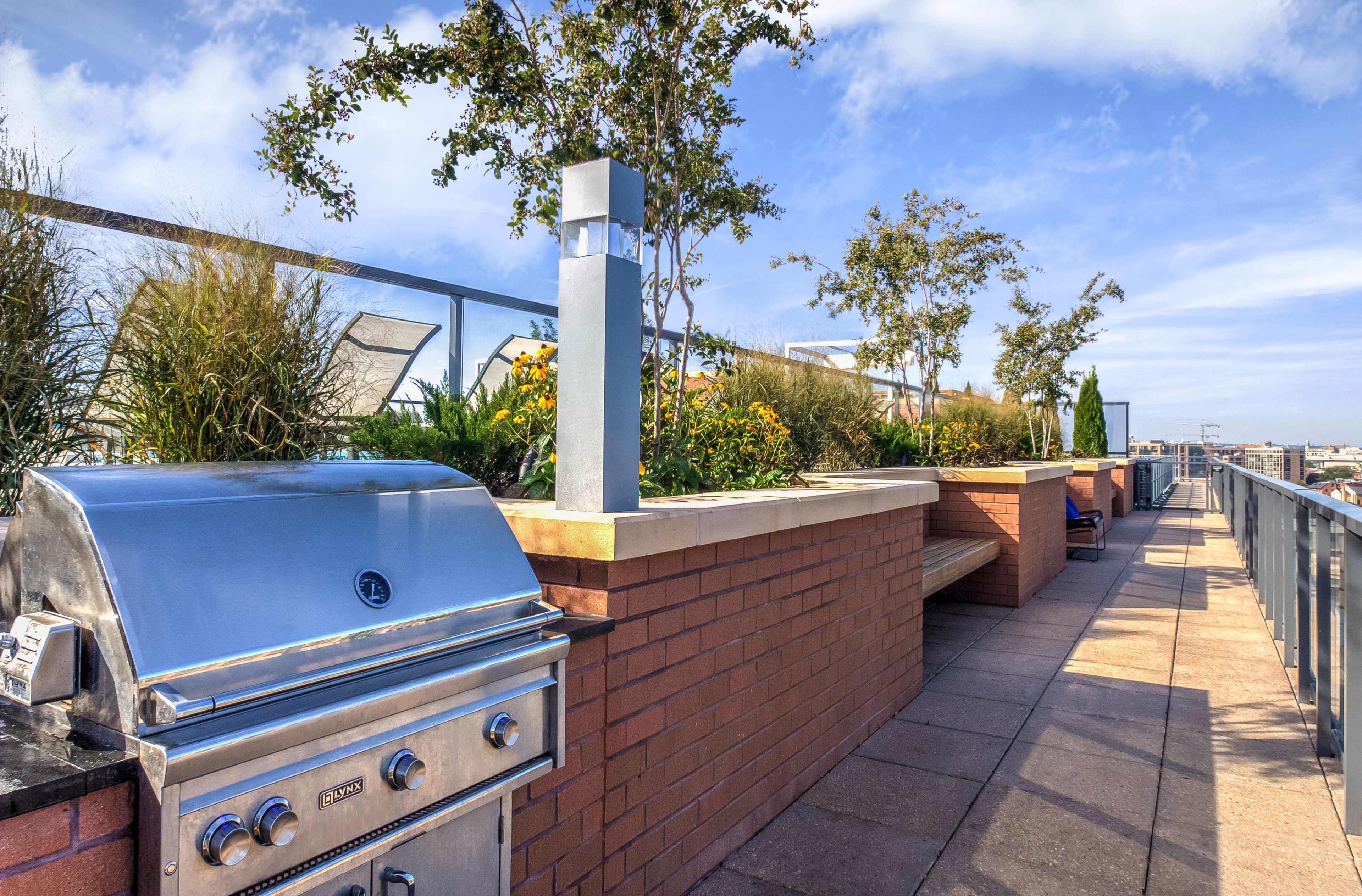 A rooftop terrace features a stainless steel grill next to planted areas with flowers and greenery.