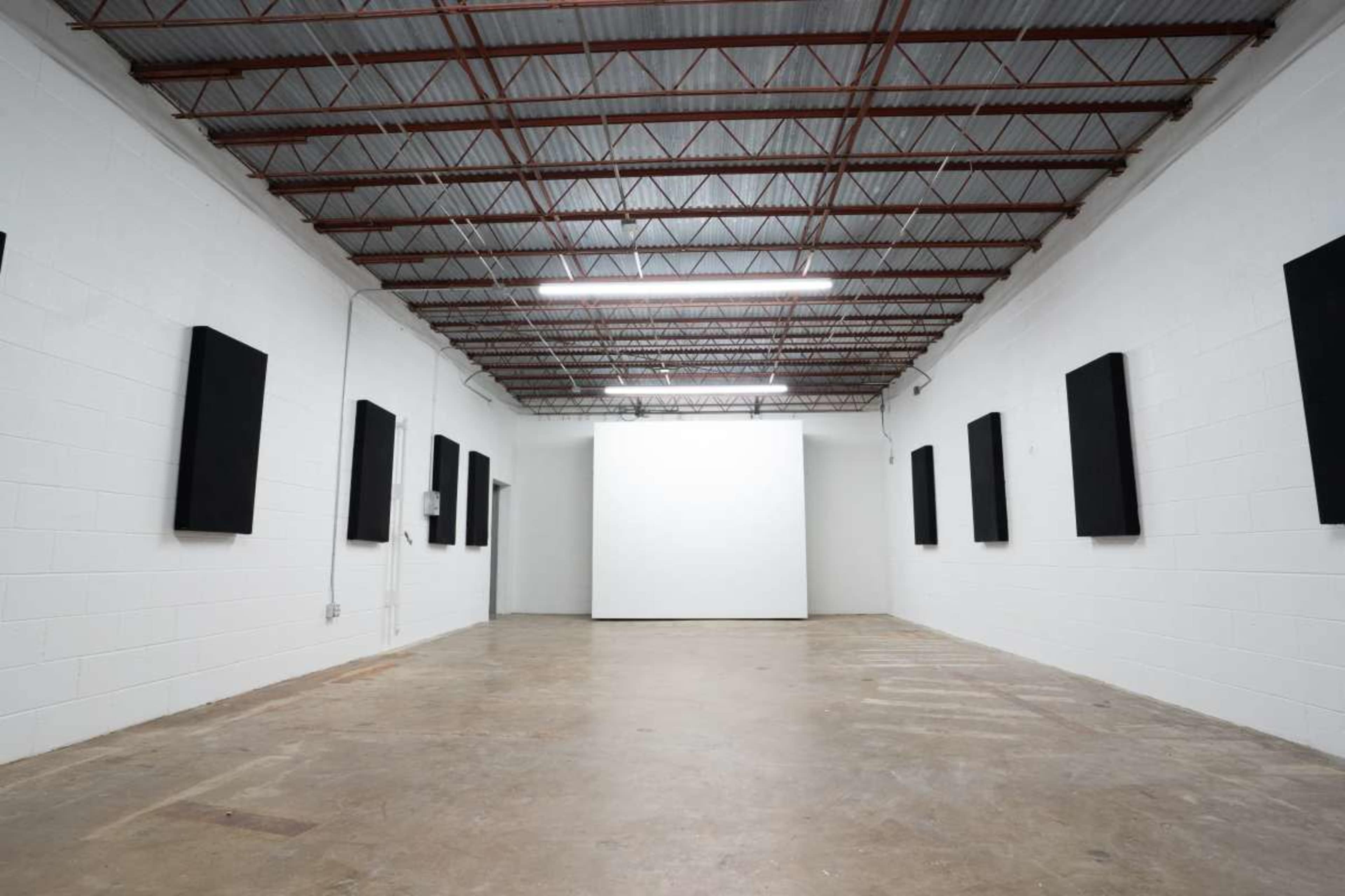 The image shows an empty gallery space with white walls and several dark panels mounted on the walls.
