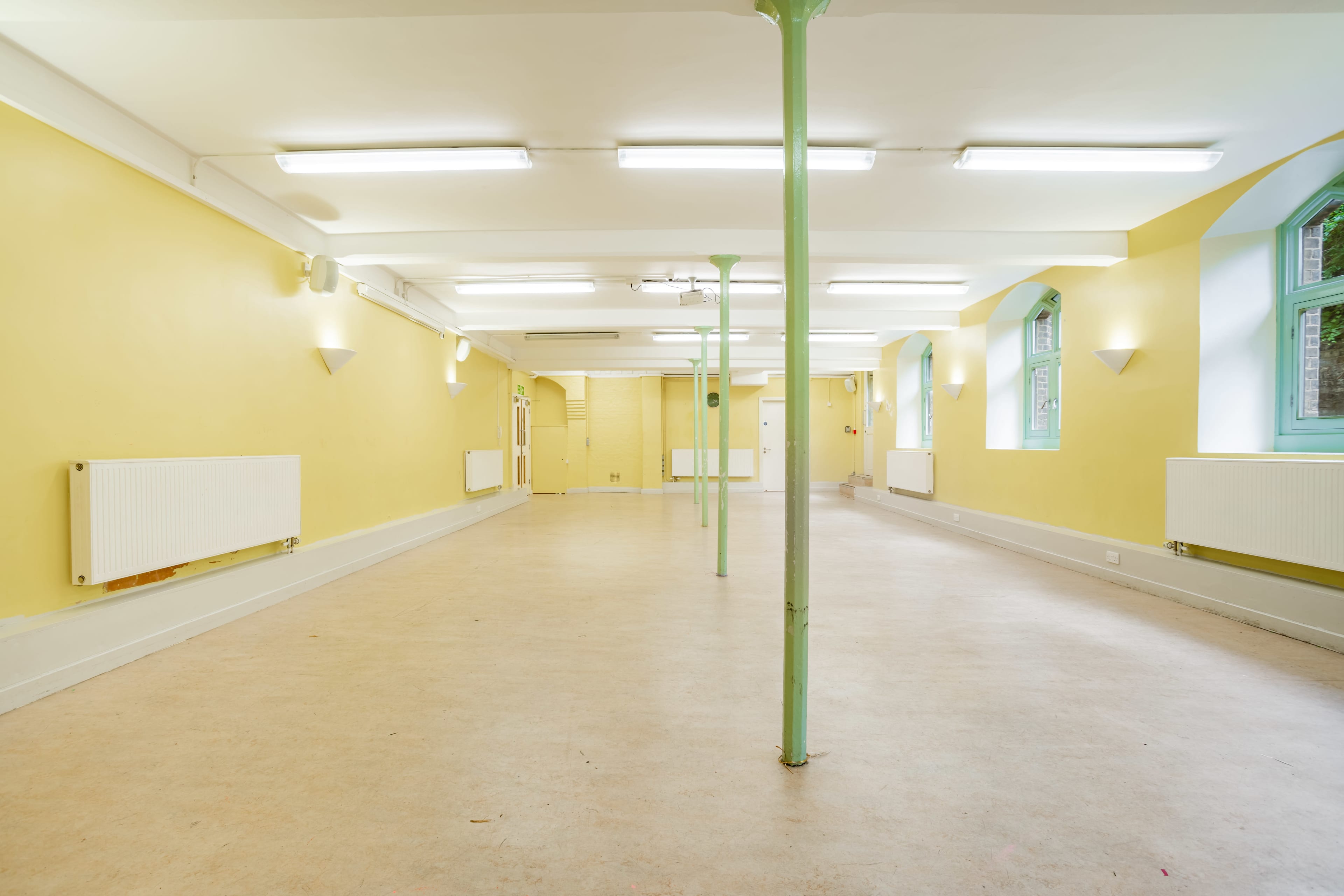 An empty room with yellow walls, a light-colored floor, and green columns supporting the ceiling.